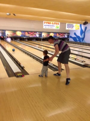 A man assists a young child as they prepare to bowl on a lane with bumpers.