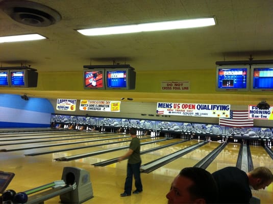 Indoor bowling alley with overhead scoring monitors and banners for upcoming tournaments and leagues.