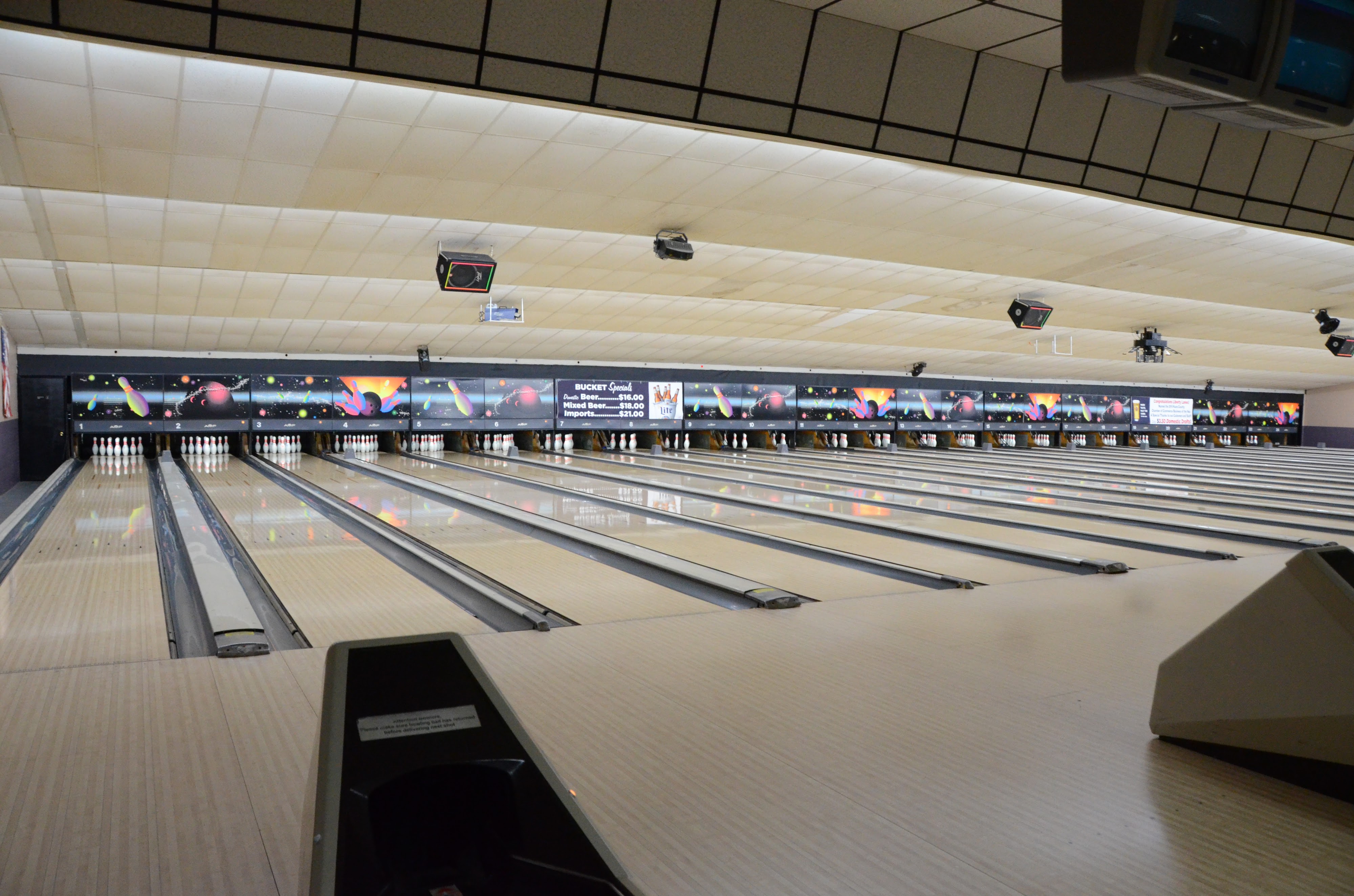 A wide view of multiple well-lit bowling lanes with colorful graphics on the masking units and pins set at the end.