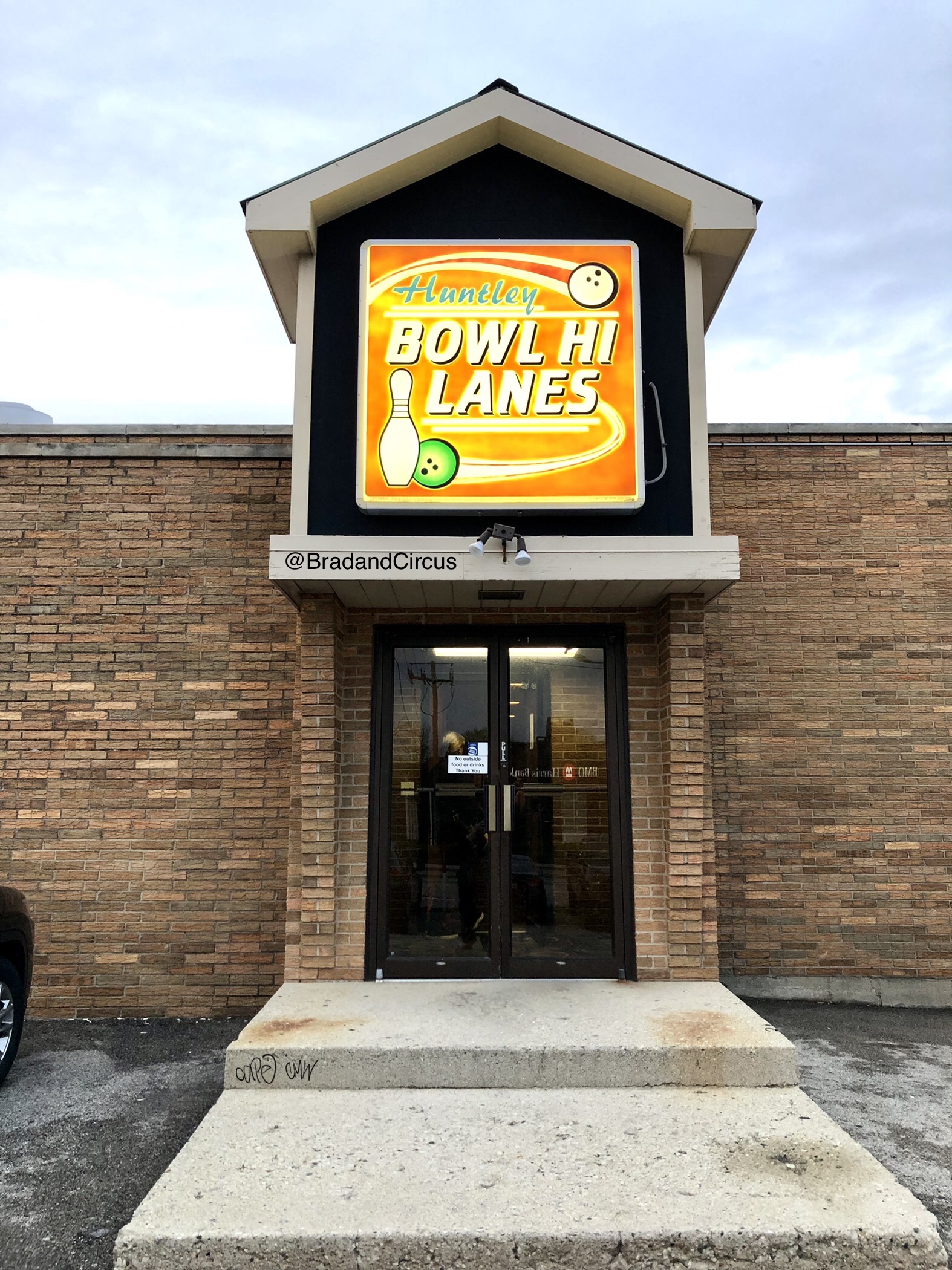 The brick exterior and main entrance of Bowl-Hi Lanes featuring a bright orange and yellow glowing sign.