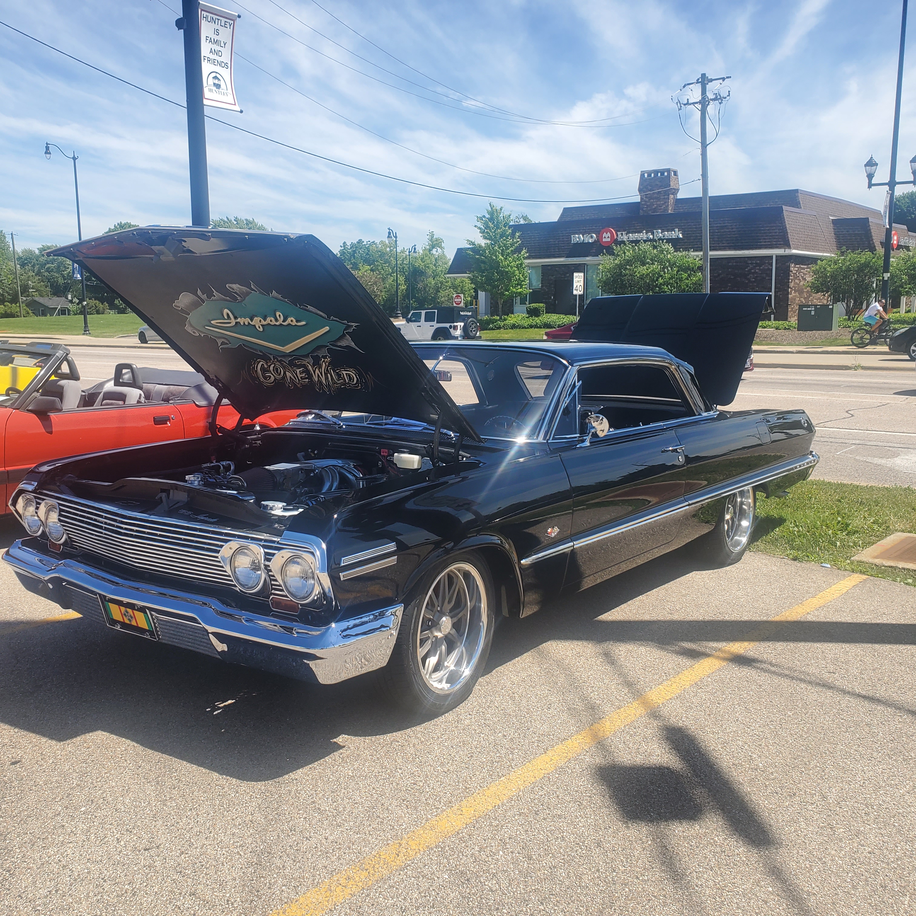 A black classic Chevrolet Impala with its hood open at an outdoor car show.