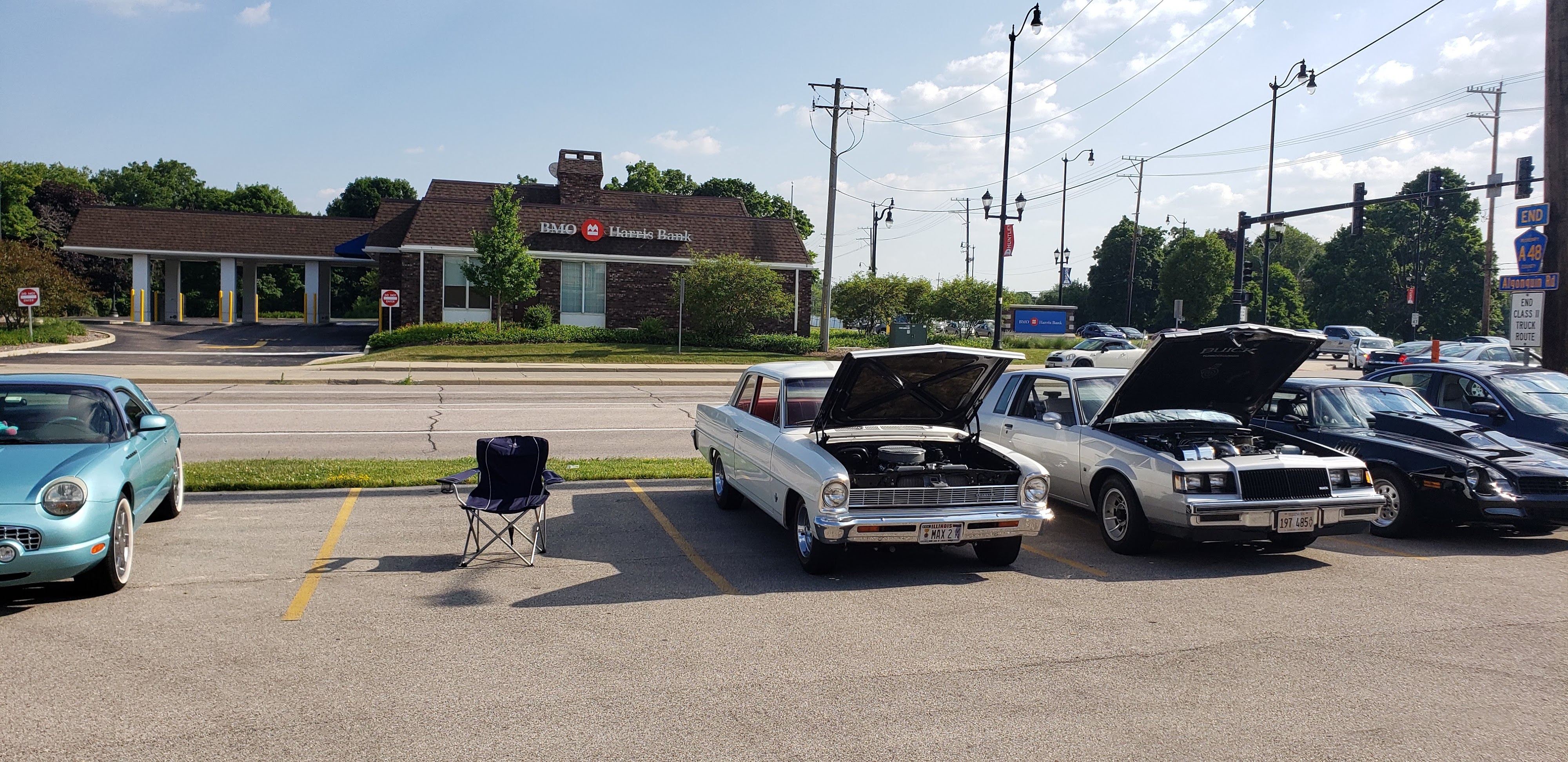 Classic cars parked with their hoods open in a sunny parking lot during a community event.