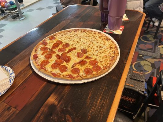 A half-pepperoni and half-cheese thin-crust pizza on a wooden table in a bowling alley.
