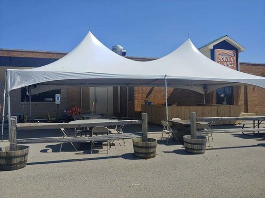 A large white event tent with a wooden bar and seating area set up outside the Bowl-Hi Lanes brick building.