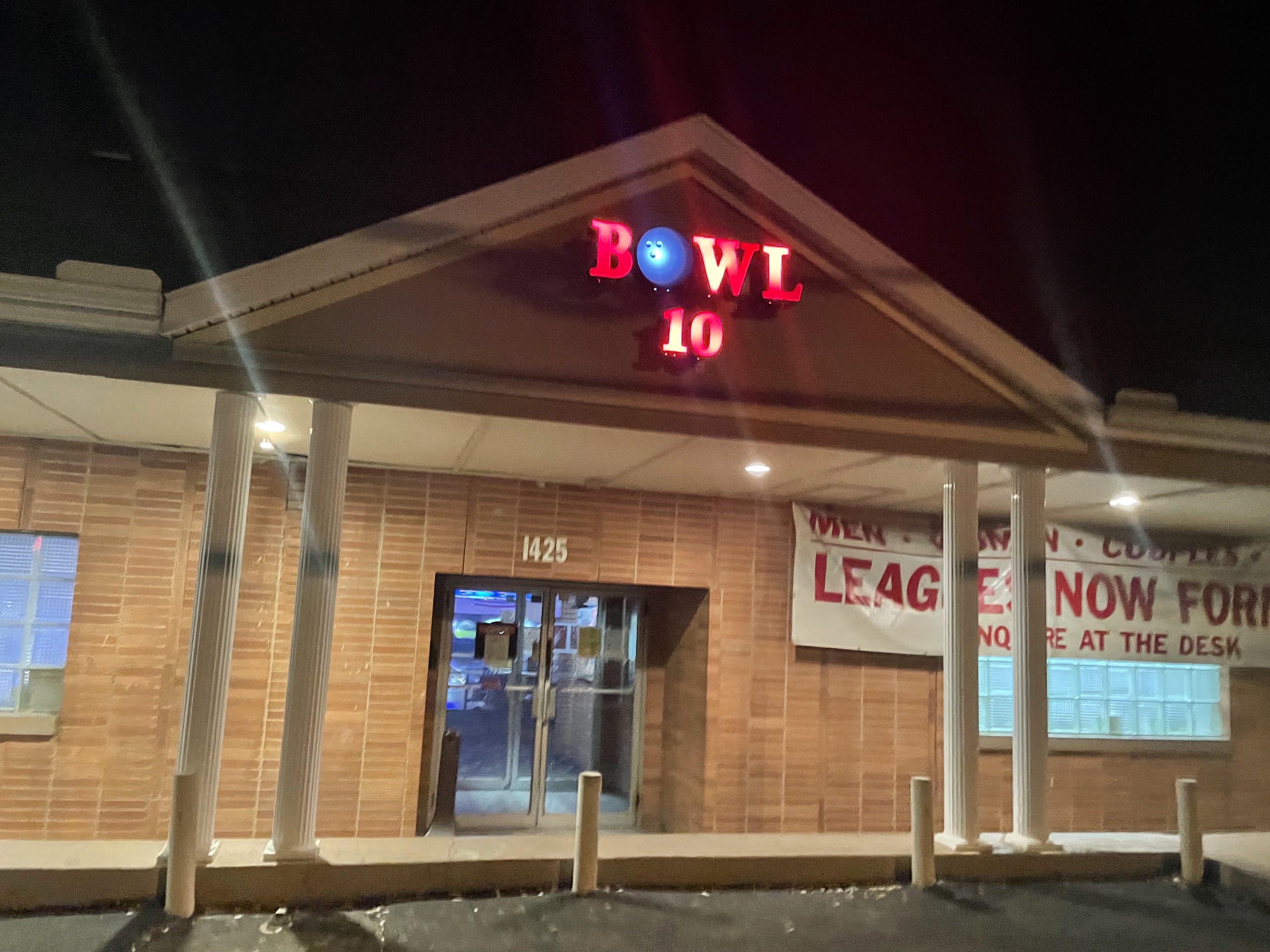 The brick exterior of Bowl 10 at night featuring a bright red neon sign and a league banner.