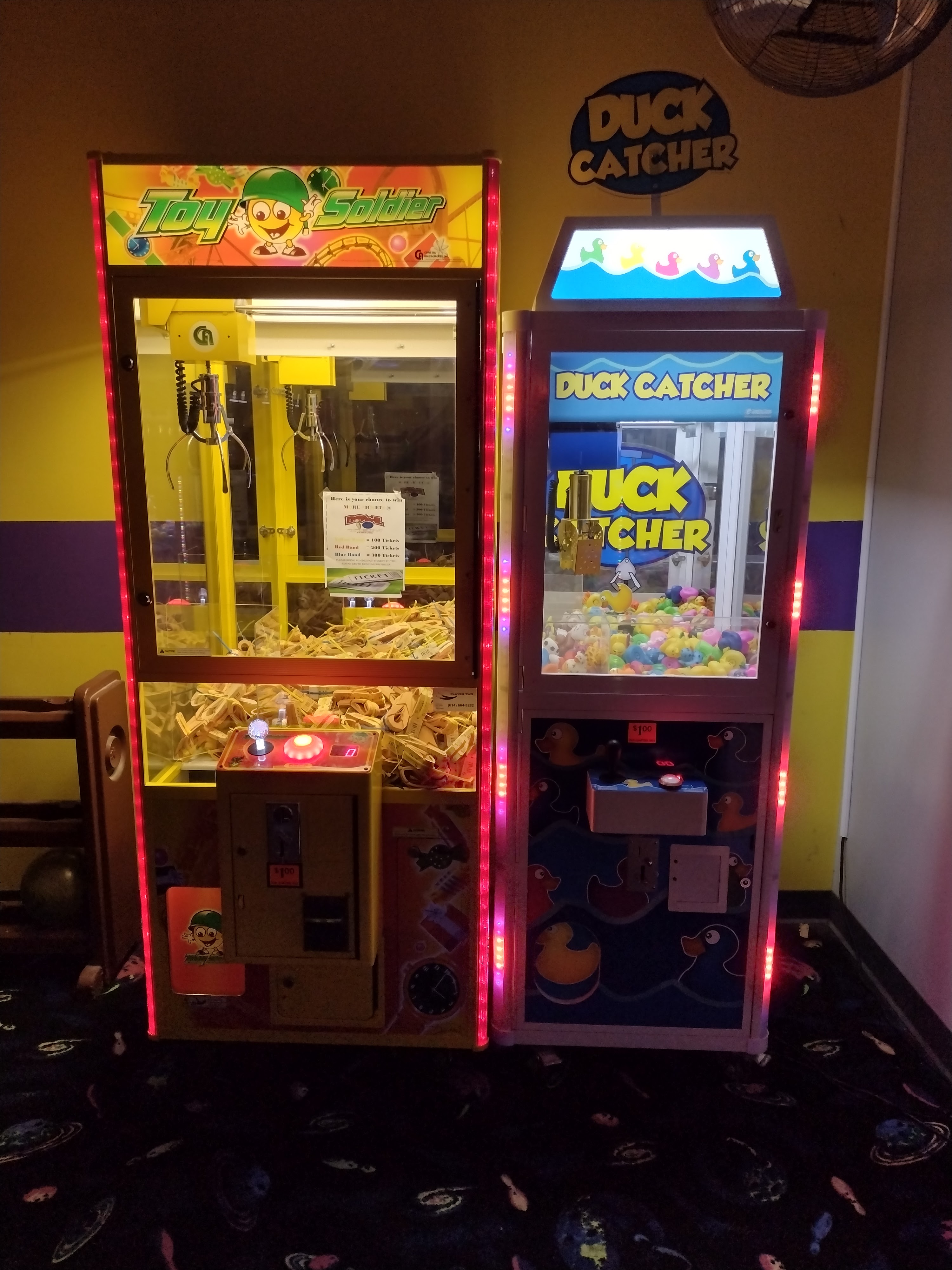 Two arcade claw machines, Toy Soldier and Duck Catcher, standing on a space-themed carpet.
