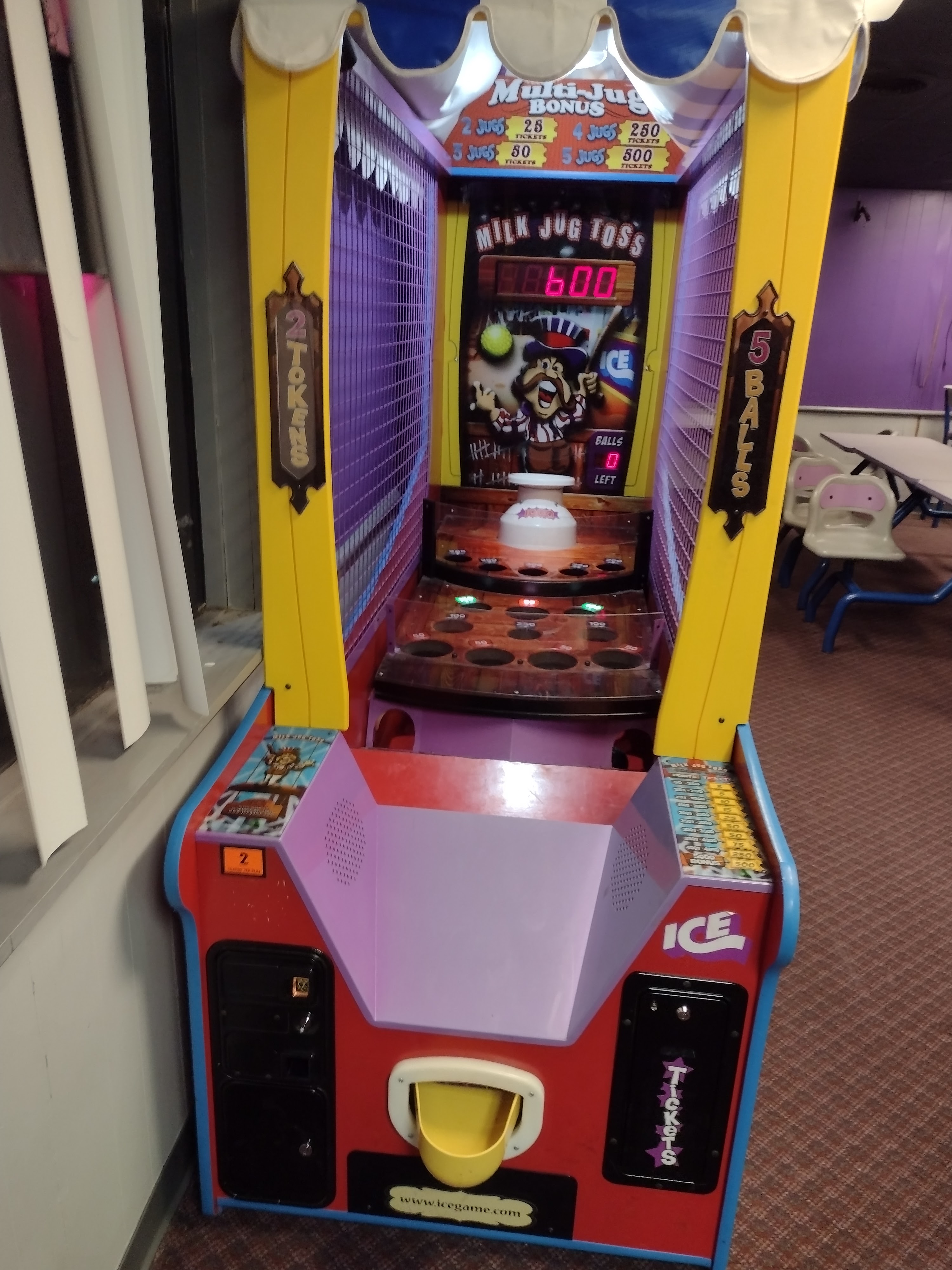 A brightly colored Milk Jug Toss arcade game cabinet with a digital scoreboard in a bowling center arcade area.
