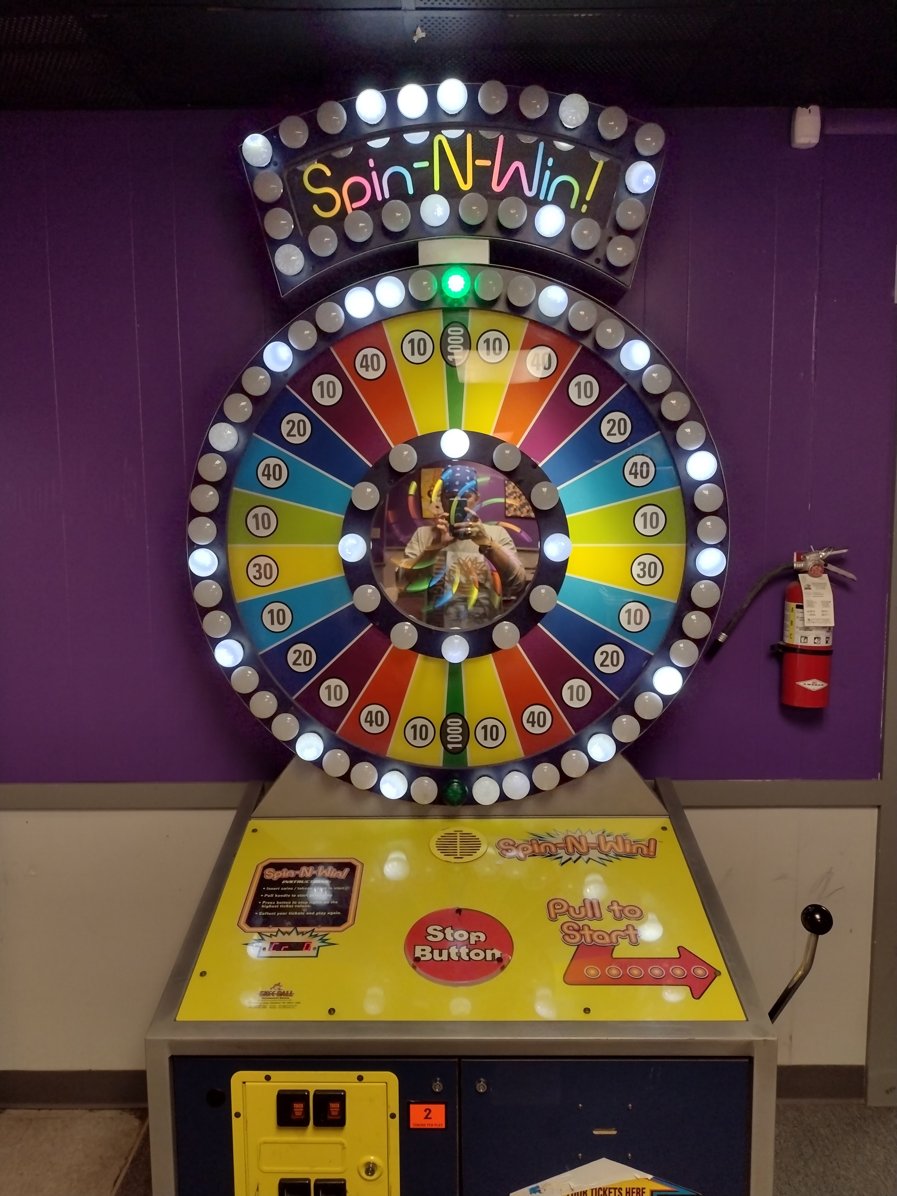A colorful Spin-N-Win arcade game with a light-up wheel and ticket prizes located against a purple wall.