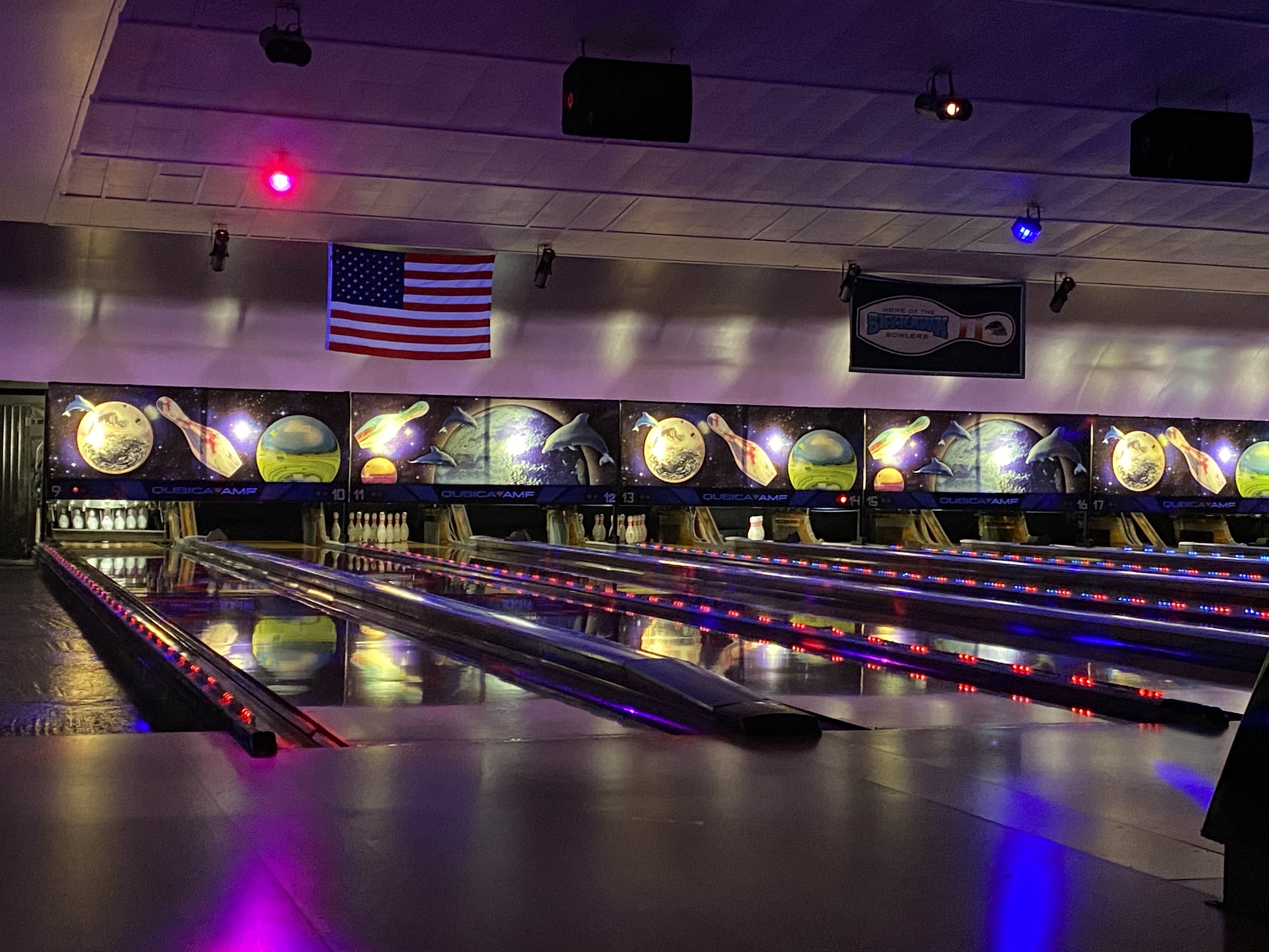 A row of bowling lanes at Bowl 10 Fairborn featuring cosmic glow lighting and space-themed murals.