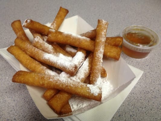 A basket of fried dough sticks topped with powdered sugar and a side of dipping syrup.