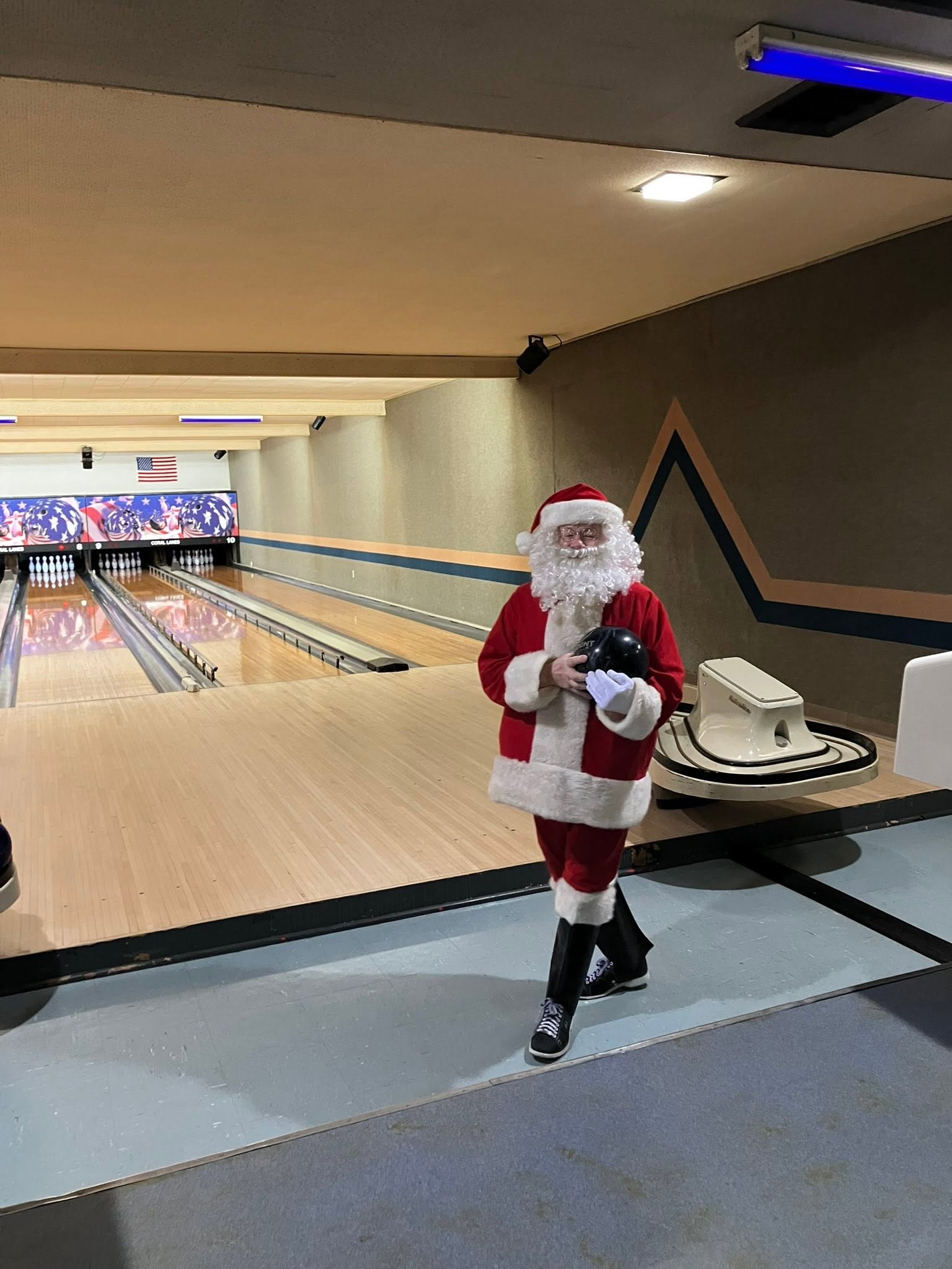 A person dressed as Santa Claus holds a bowling ball while standing on a bowling lane.