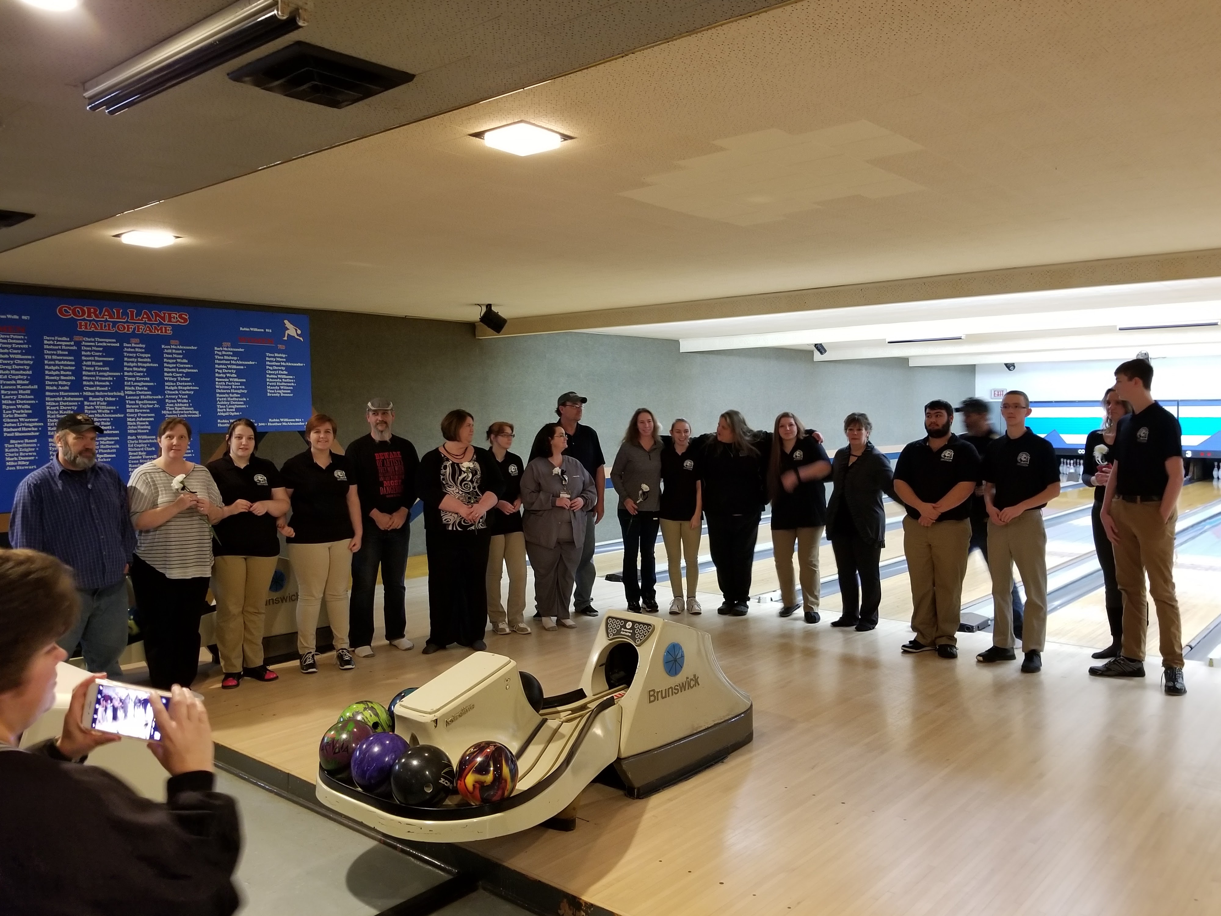 A large group of people posing for a photo on bowling lanes next to a Hall of Fame board.