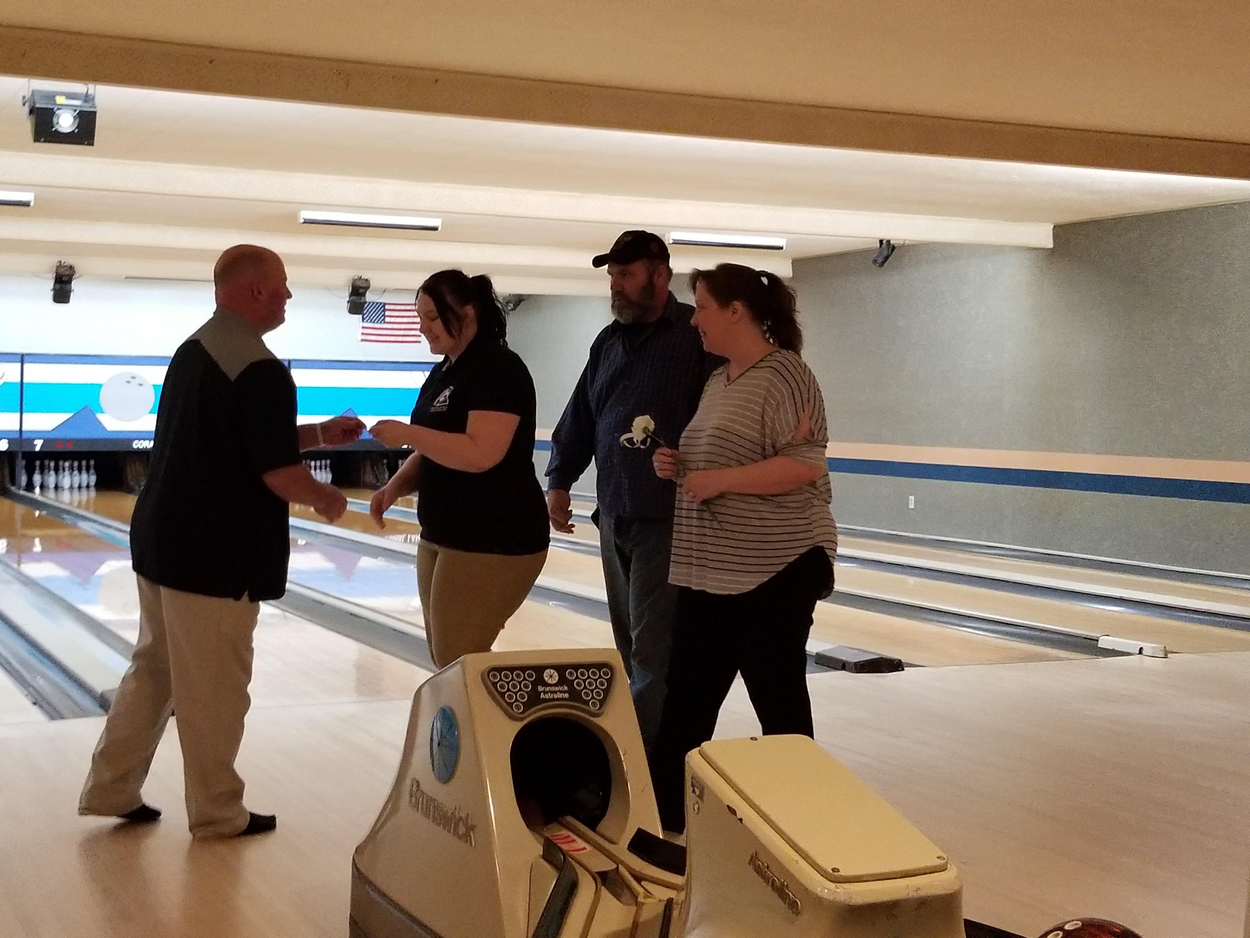 Four people stand and socialize on a bowling lane approach near a ball return.