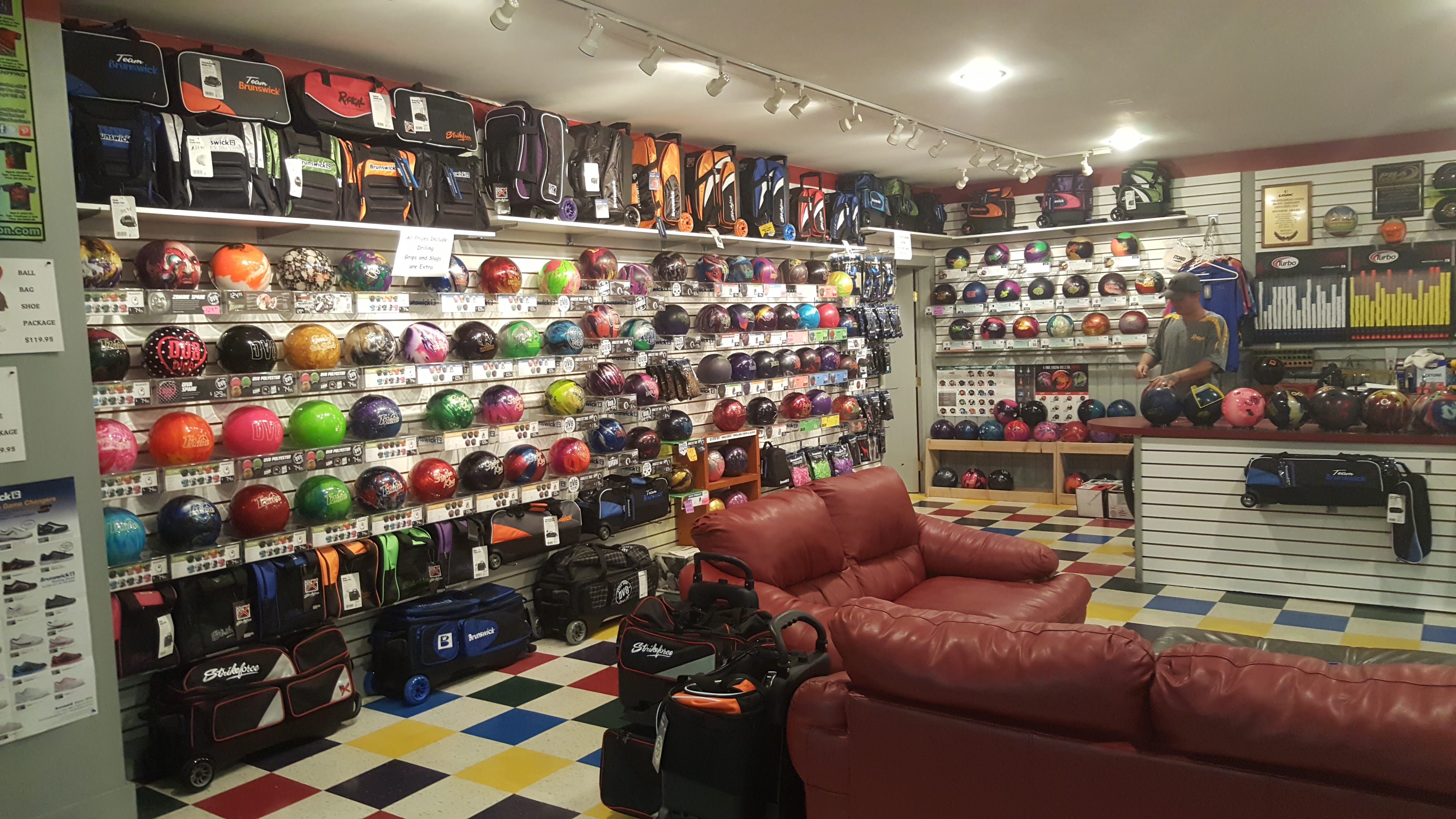 A bowling pro shop with rows of colorful bowling balls on wall displays and red leather sofas in the foreground.