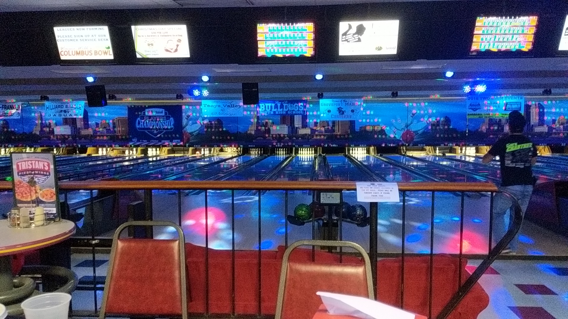 Indoor bowling lanes featuring cosmic blue lighting and overhead scoring monitors.