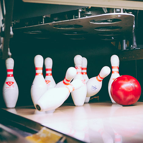 A red bowling ball strikes white pins at the end of a lane, with the pinsetter visible above.