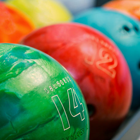 A close-up photo of colorful bowling balls including a green ball numbered 14 and a red ball numbered 12.