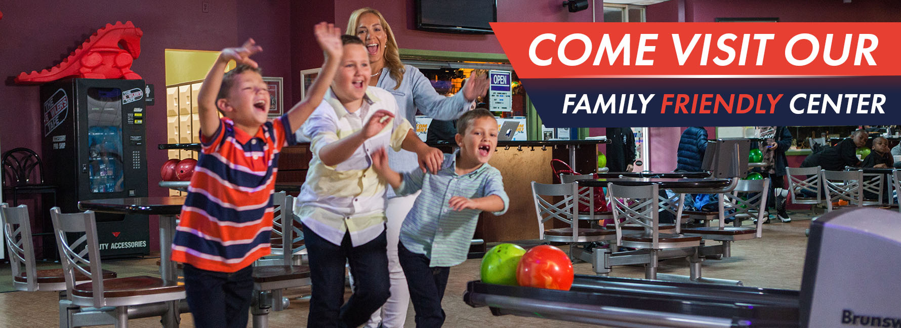 A woman and three boys celebrate at a bowling lane with a banner inviting visitors to the family friendly center.