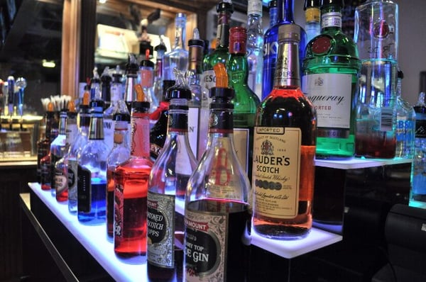 A close-up view of diverse liquor bottles arranged on a tiered, backlit bar shelf.
