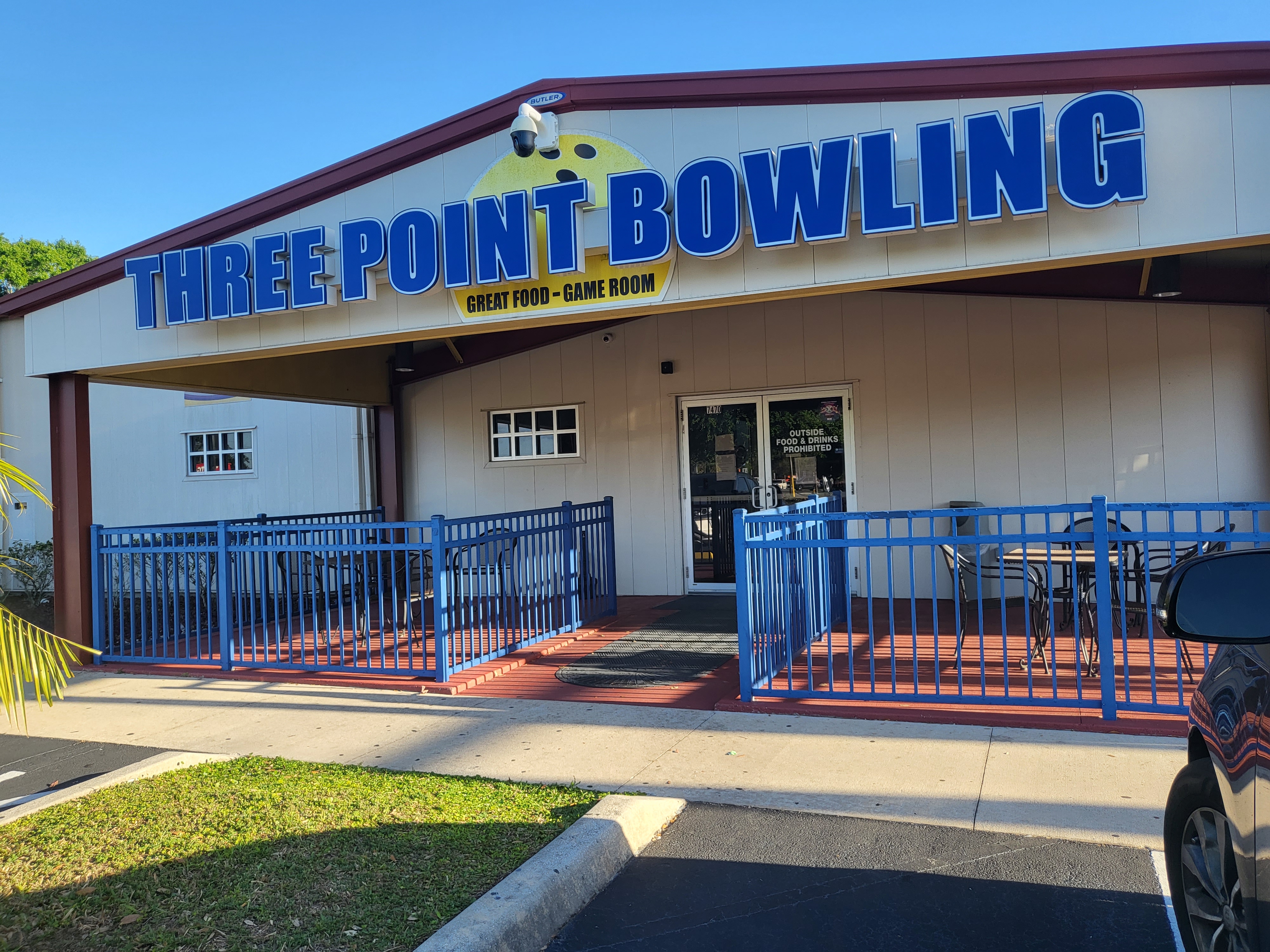 The exterior entrance of Three Point Bowling with a large blue sign and a blue-fenced patio area.