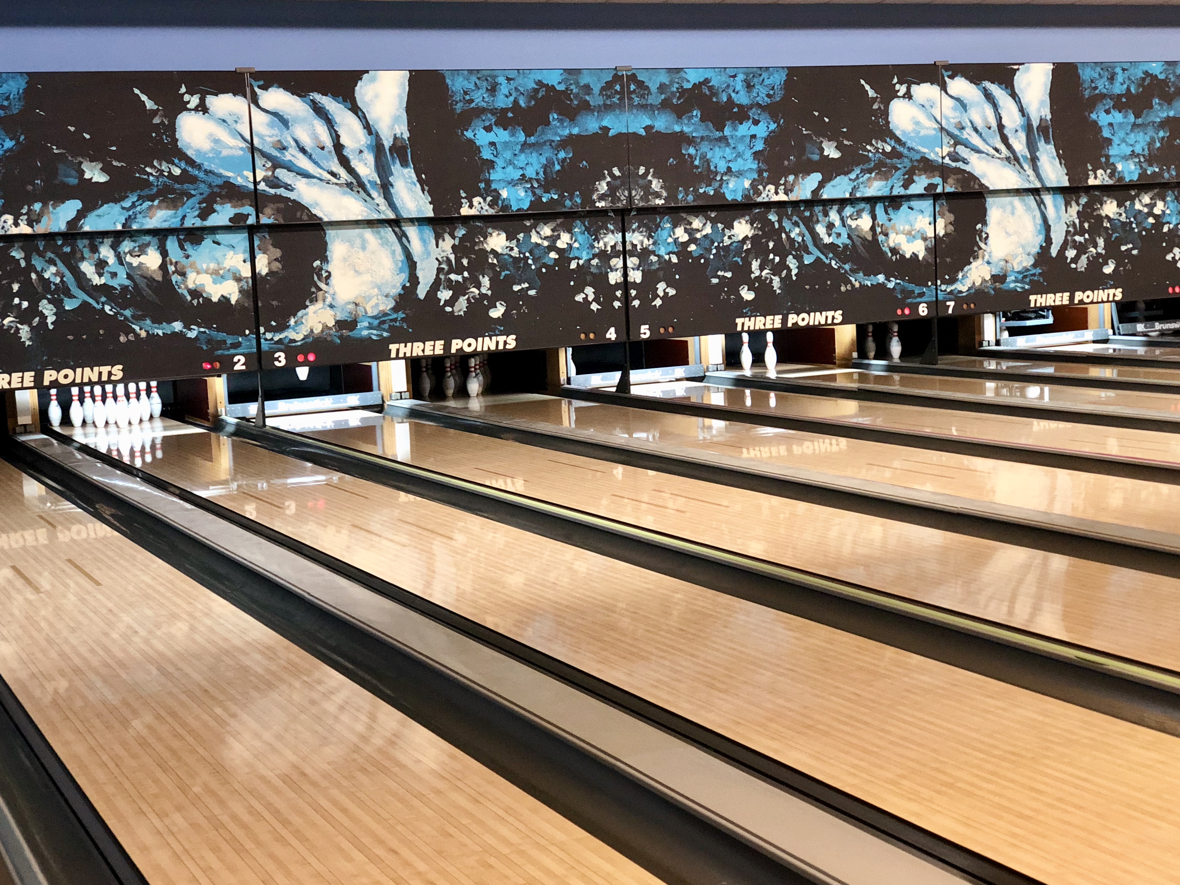 Seven bowling lanes with blue and white abstract masking units and the words Three Points above the pins.