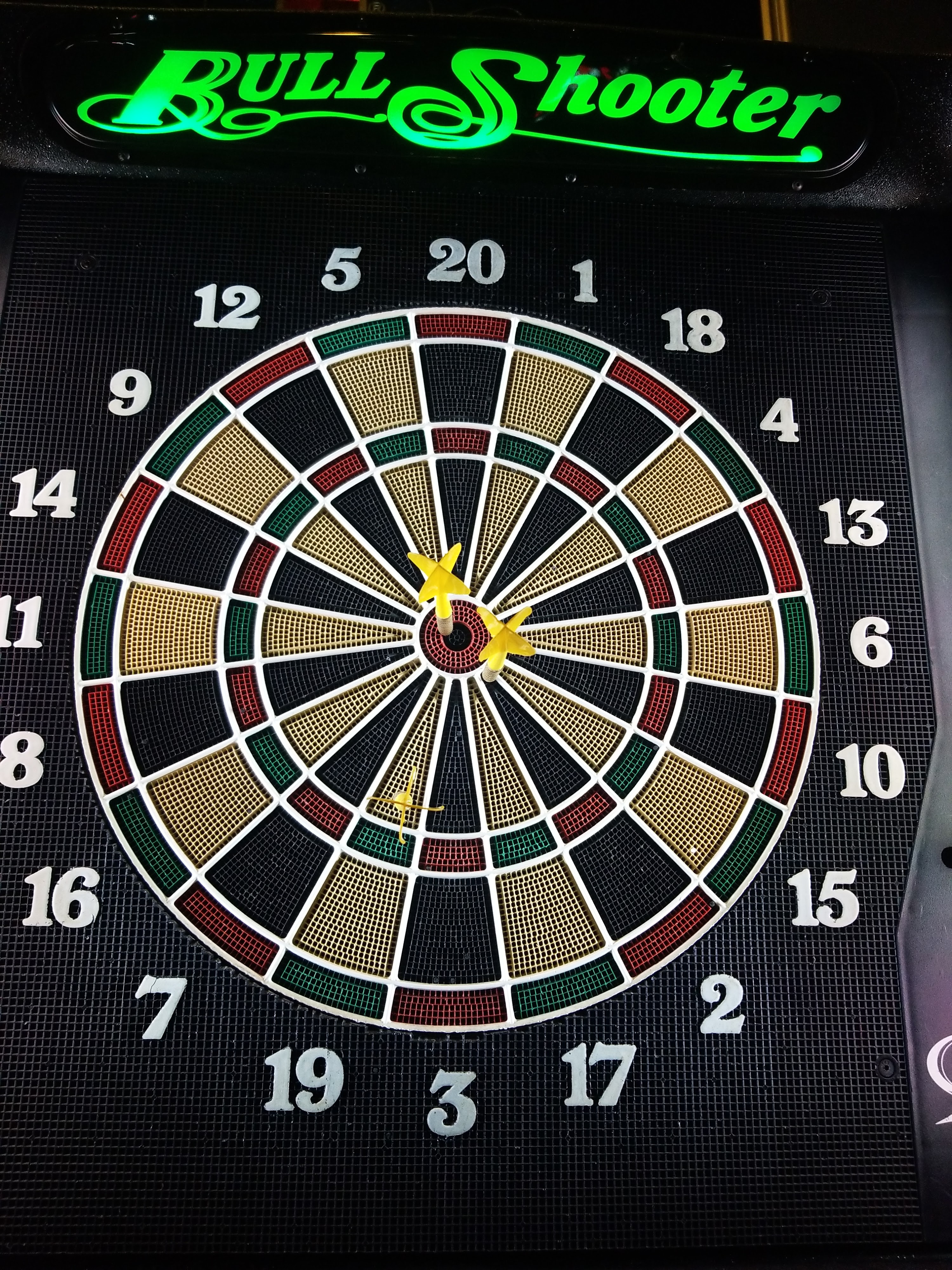 Close-up of an electronic BullShooter dartboard with three yellow darts.