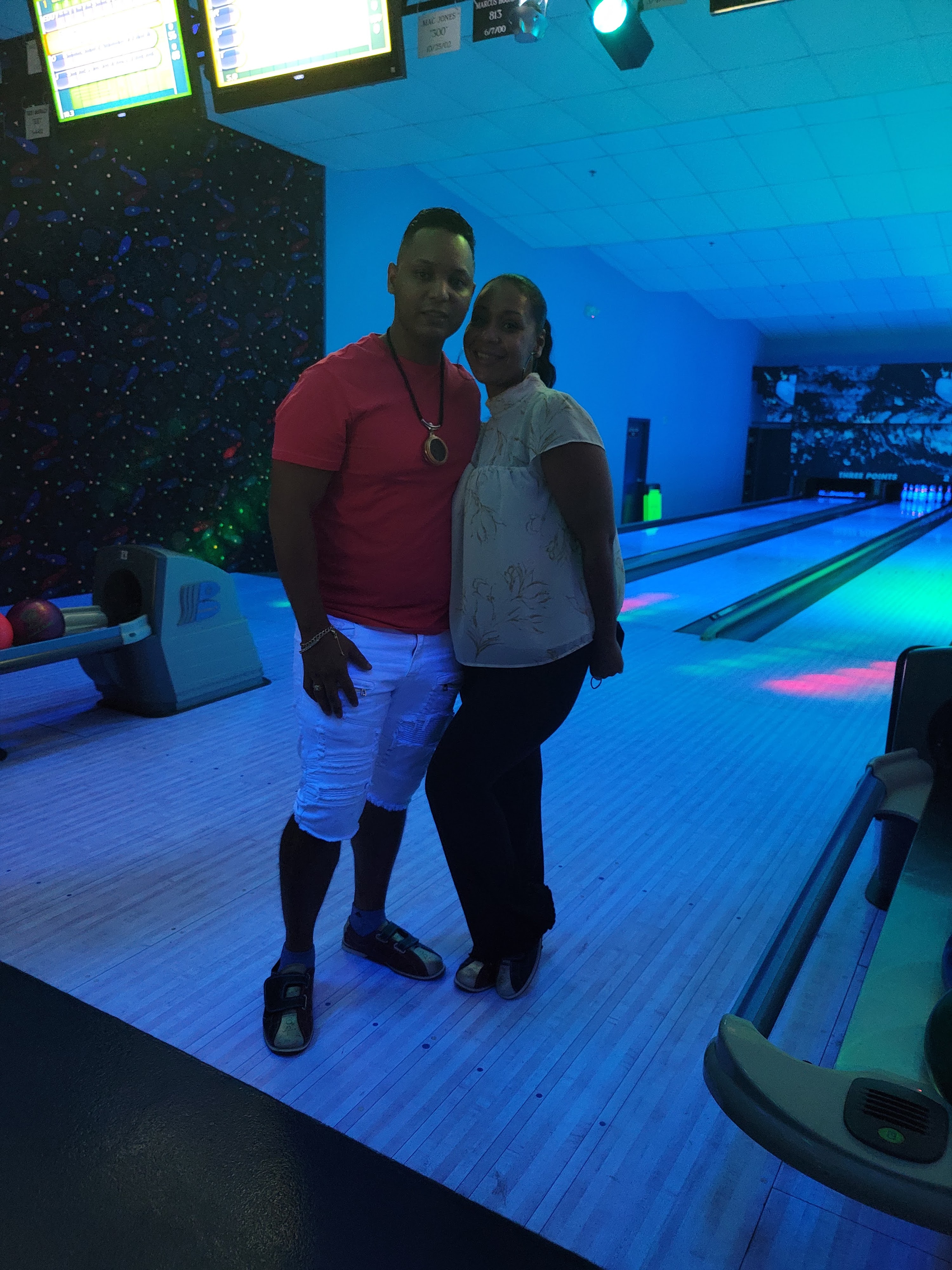 A man and woman posing on a bowling lane under blue cosmic glow lighting.