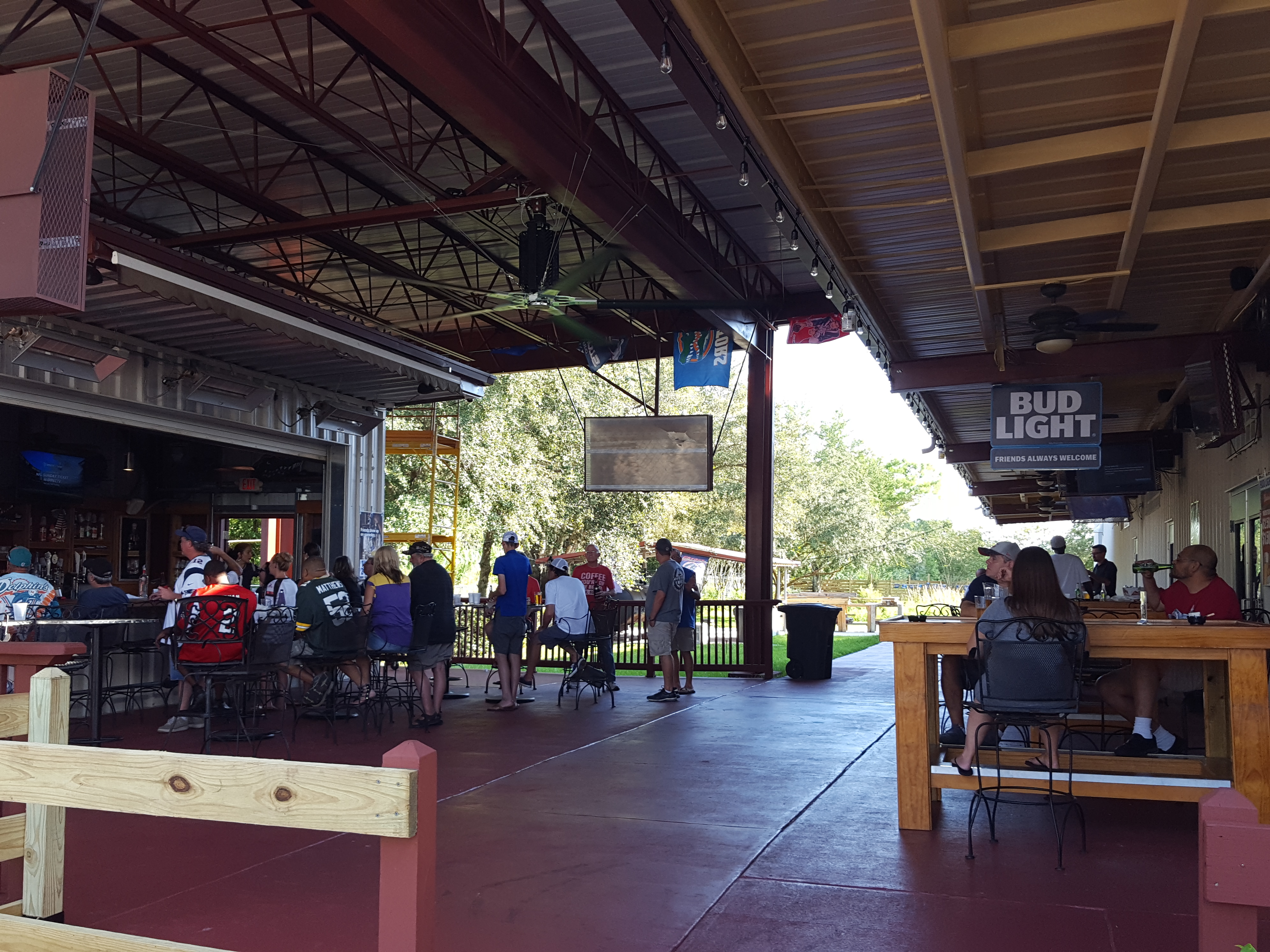 A busy outdoor covered patio bar with people sitting at high-top tables and a long service counter.
