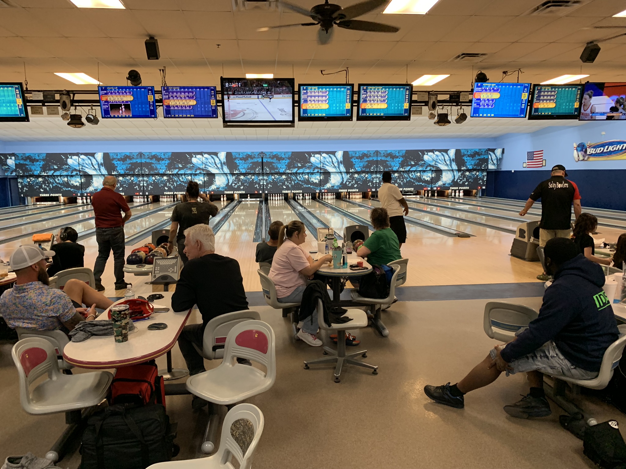 Several people bowling on well-lit lanes with digital scoreboards and wave-patterned backdrops.