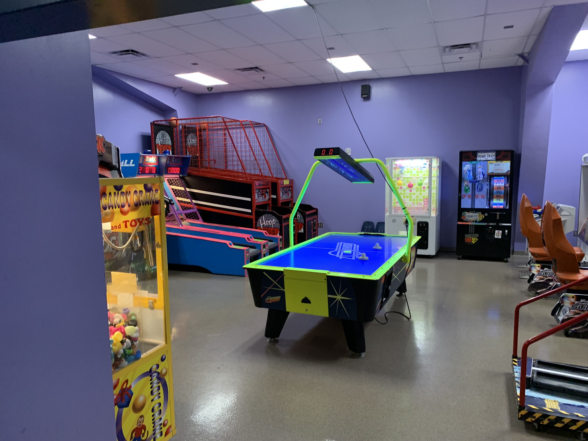 An indoor arcade featuring an air hockey table, basketball shooting games, and claw machines with plush prizes.