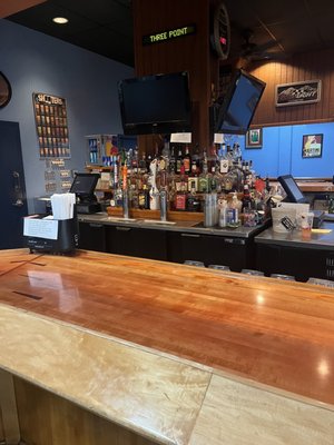 A clean, well-stocked bar with a polished wood countertop and televisions at Three Point Bowling.