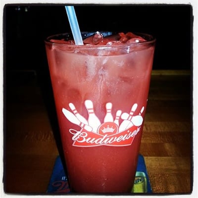 A red drink with ice and a straw in a glass featuring bowling pins and the Budweiser logo on a wooden bar.