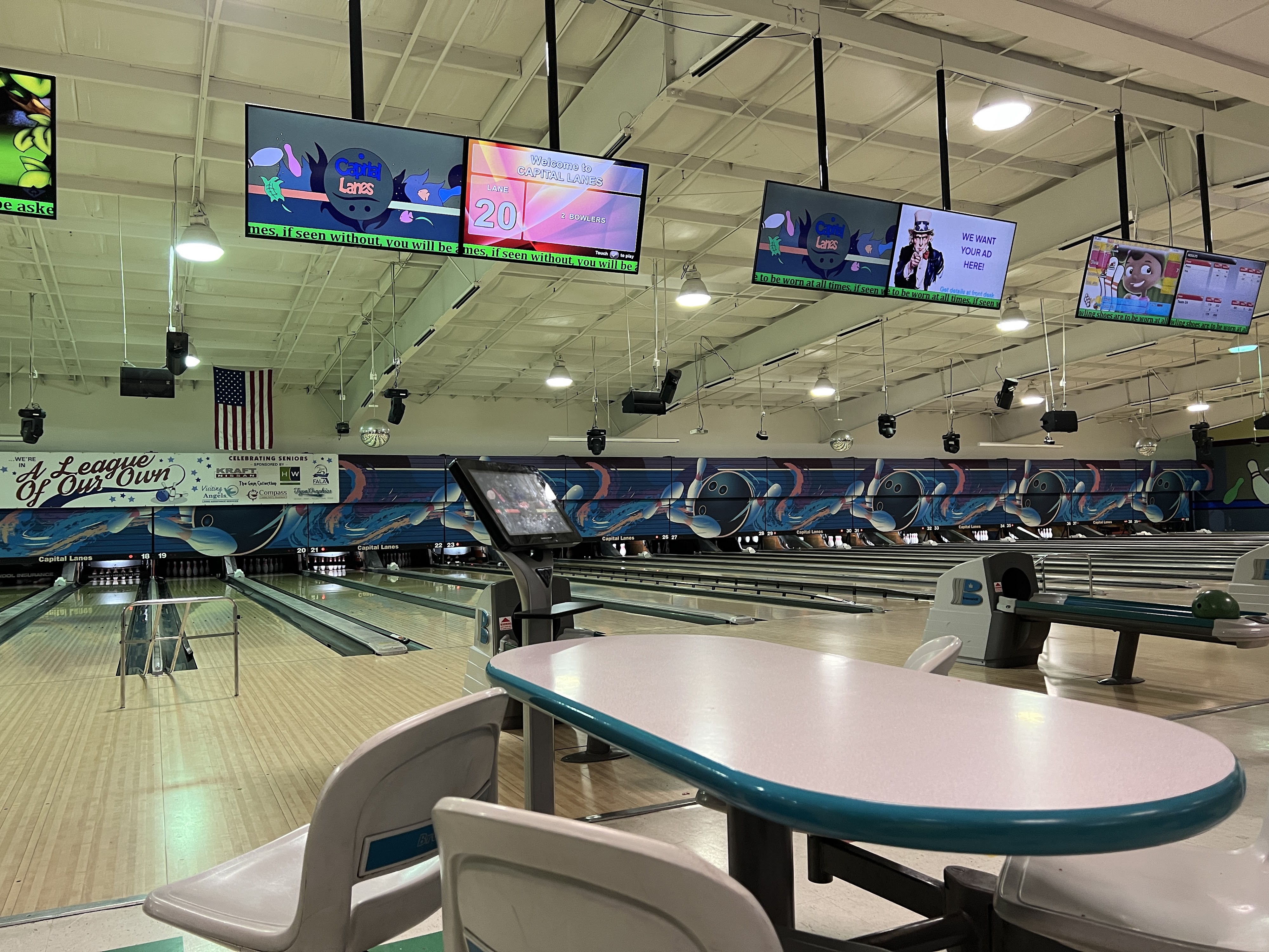 Interior view of bowling lanes at Capital Lanes with automatic scoring monitors and seating in the foreground.