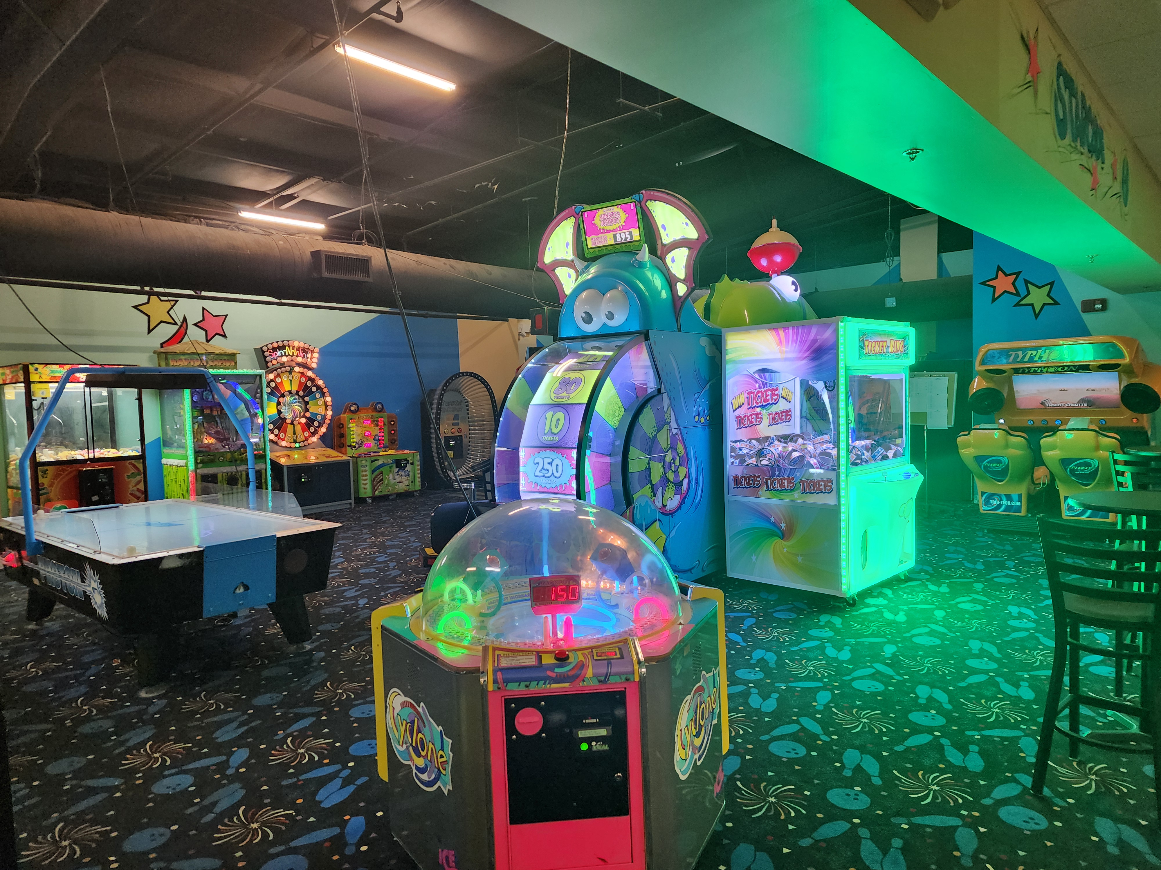 A brightly lit arcade room with an air hockey table, ticket redemption games, and a racing simulator.