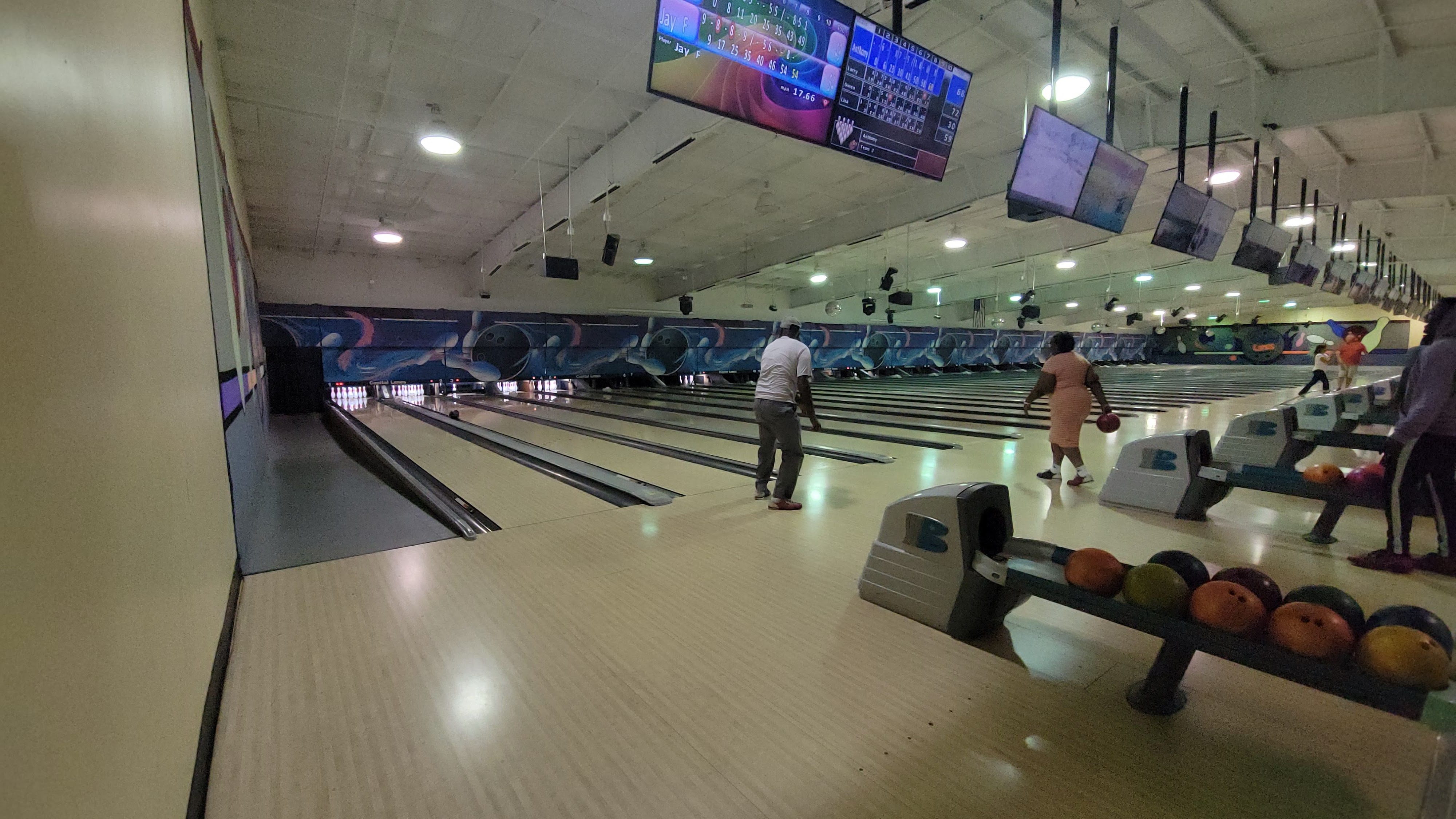 Several people bowling on modern lanes with large digital scoring monitors overhead.