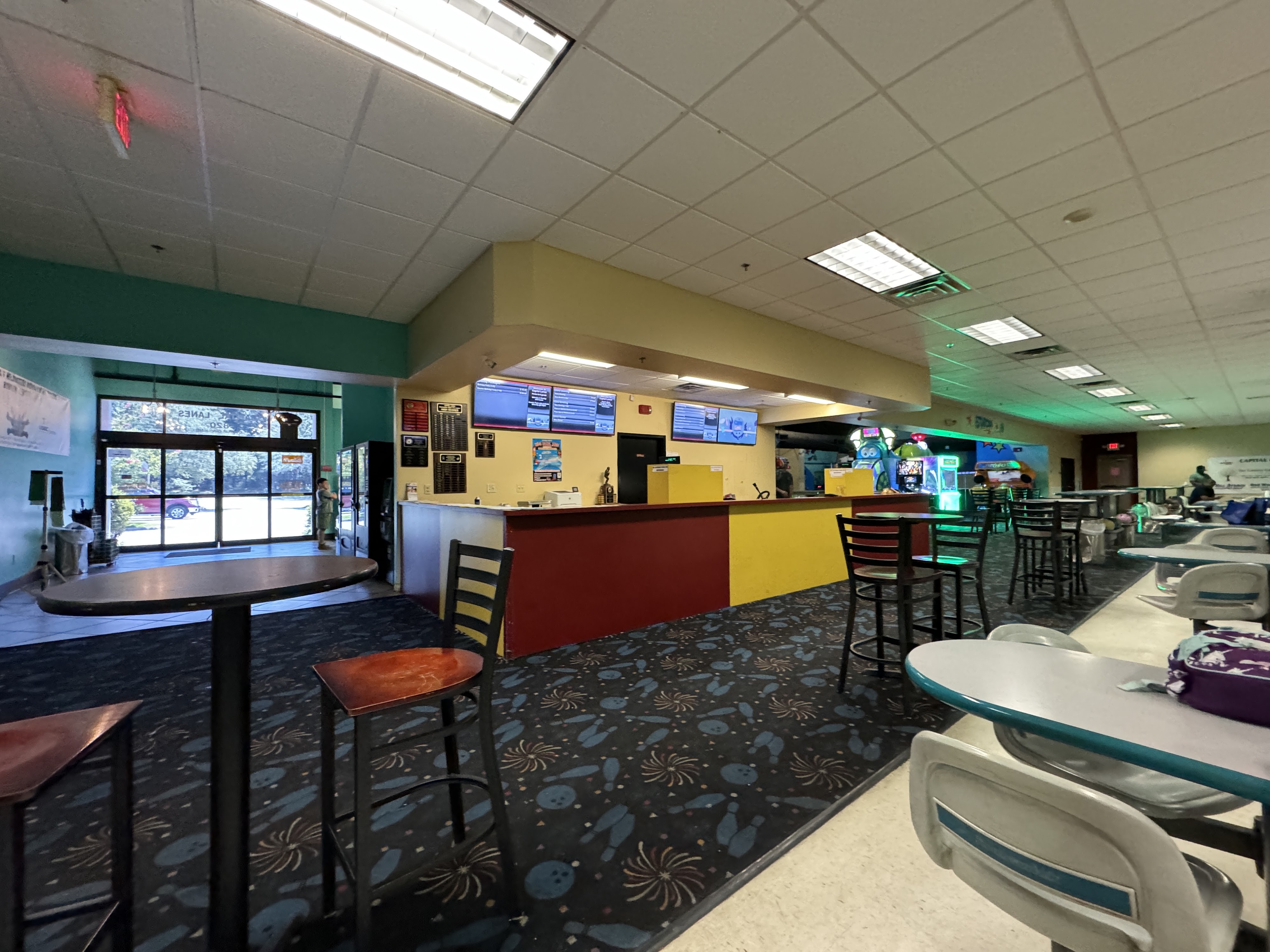 A bowling alley check-in counter with red and yellow panels and high-top tables in the foreground.
