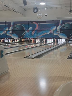 A wide view of polished bowling lanes with blue ball and pin graphics above the pins at Capital Lanes.
