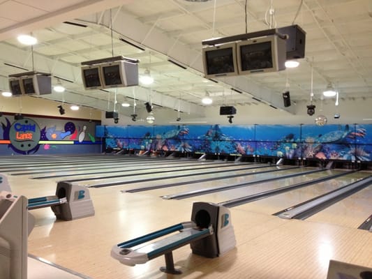 An empty bowling center with several lanes, overhead scoring monitors, and an underwater mural of sea turtles.