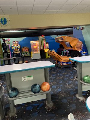A view from the bowling lanes looking into an arcade area with various game machines and a racing simulator.