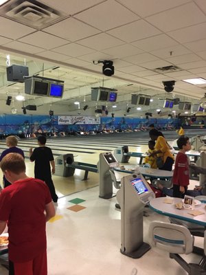 Children and adults socialising and bowling at a brightly lit bowling alley with automatic scoring consoles.