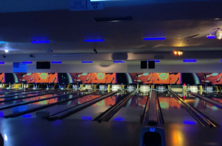 Multiple bowling lanes at Little River Lanes glowing under blue cosmic lighting with pins set and ready for play.