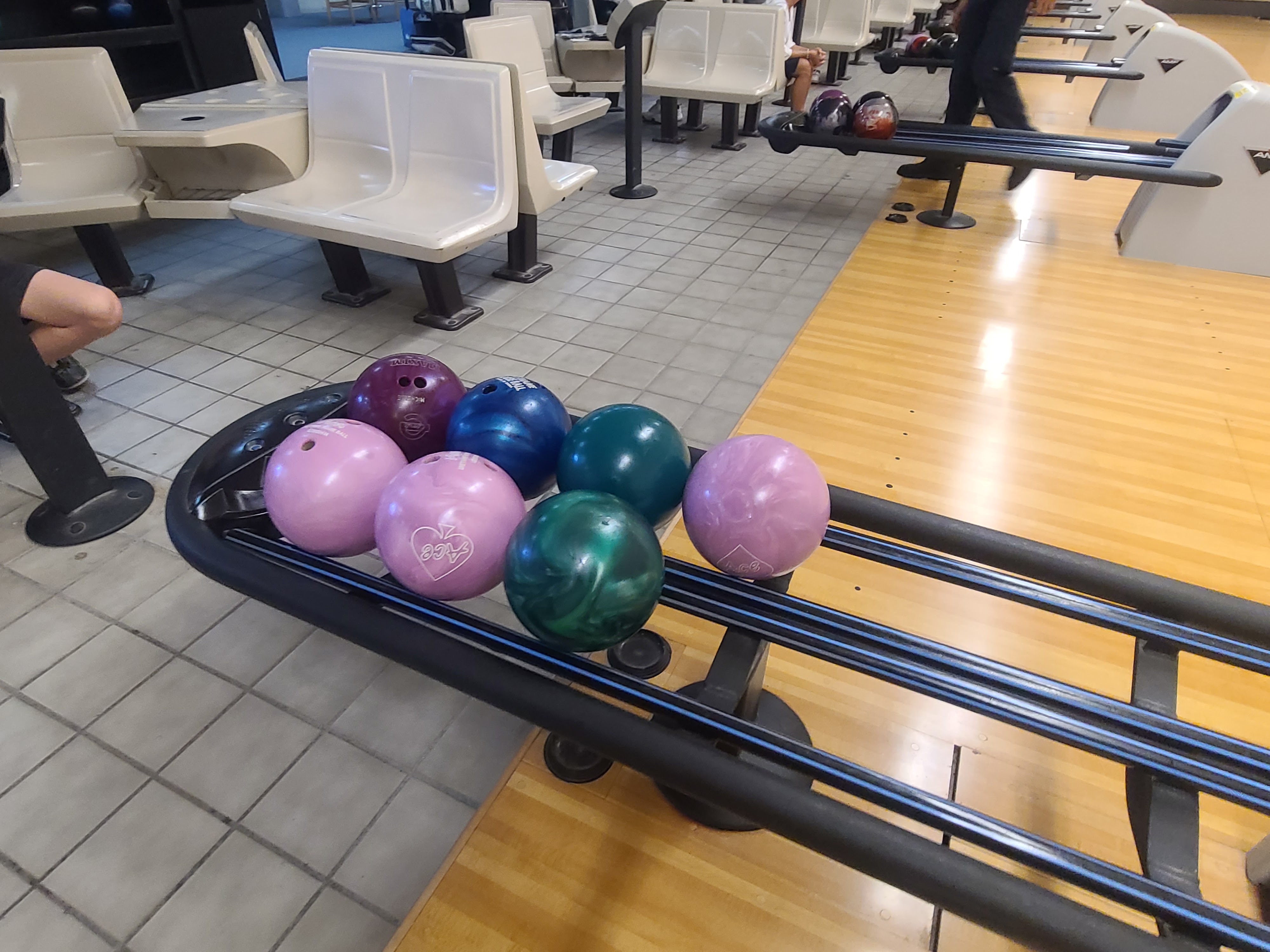 A close-up of colorful bowling balls on a ball return rack next to polished wooden lanes.
