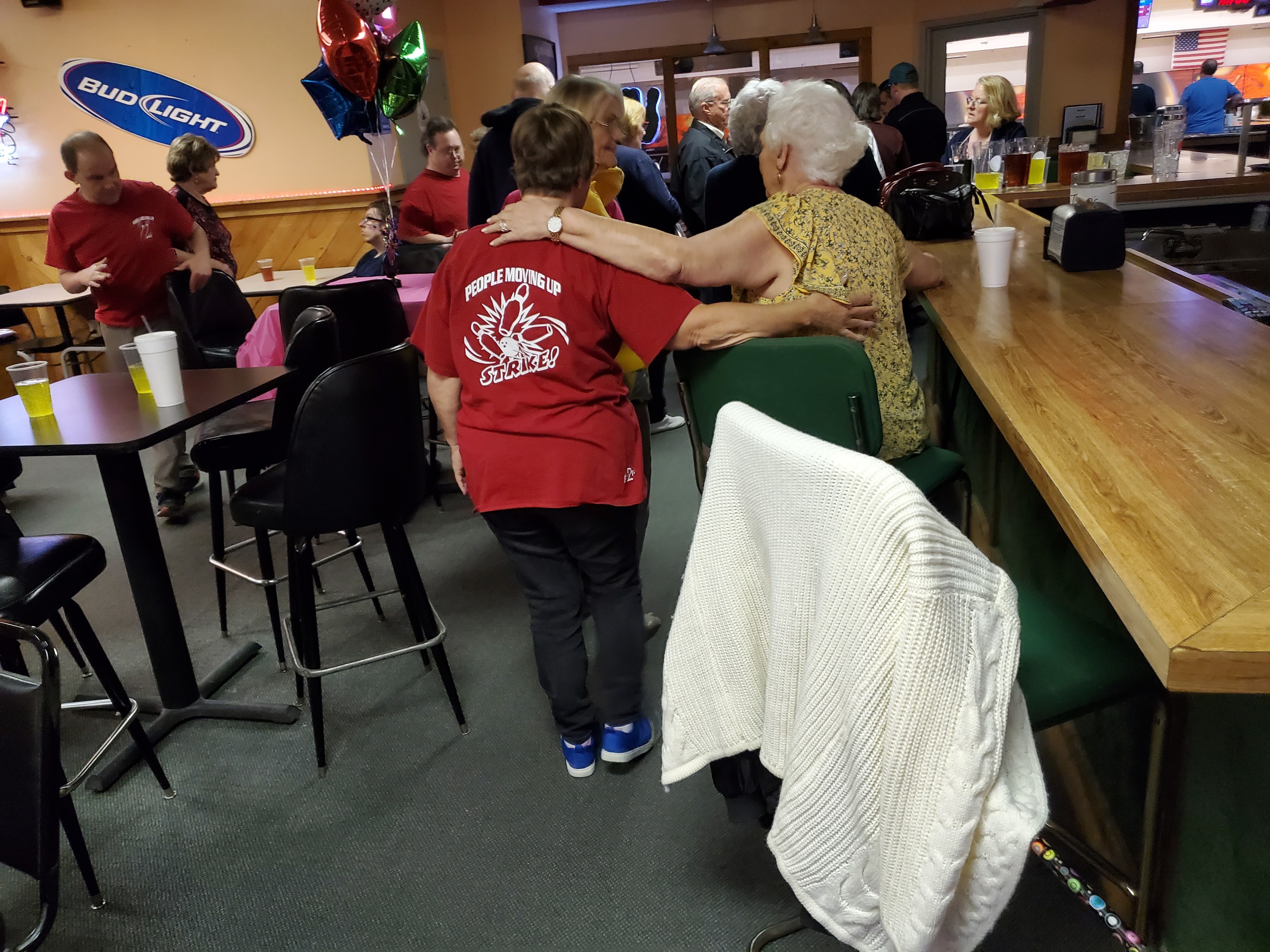 Patrons socializing and hugging in the bar and lounge area of a bowling center.