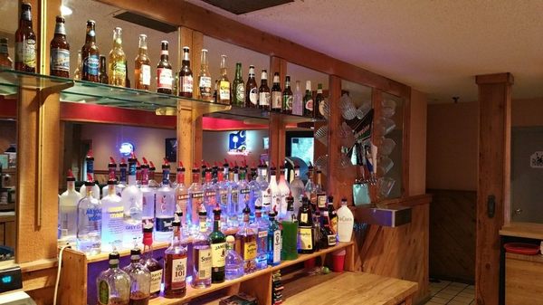 A well-stocked bar featuring rows of liquor bottles with blue under-lighting and various beer bottles on a shelf.