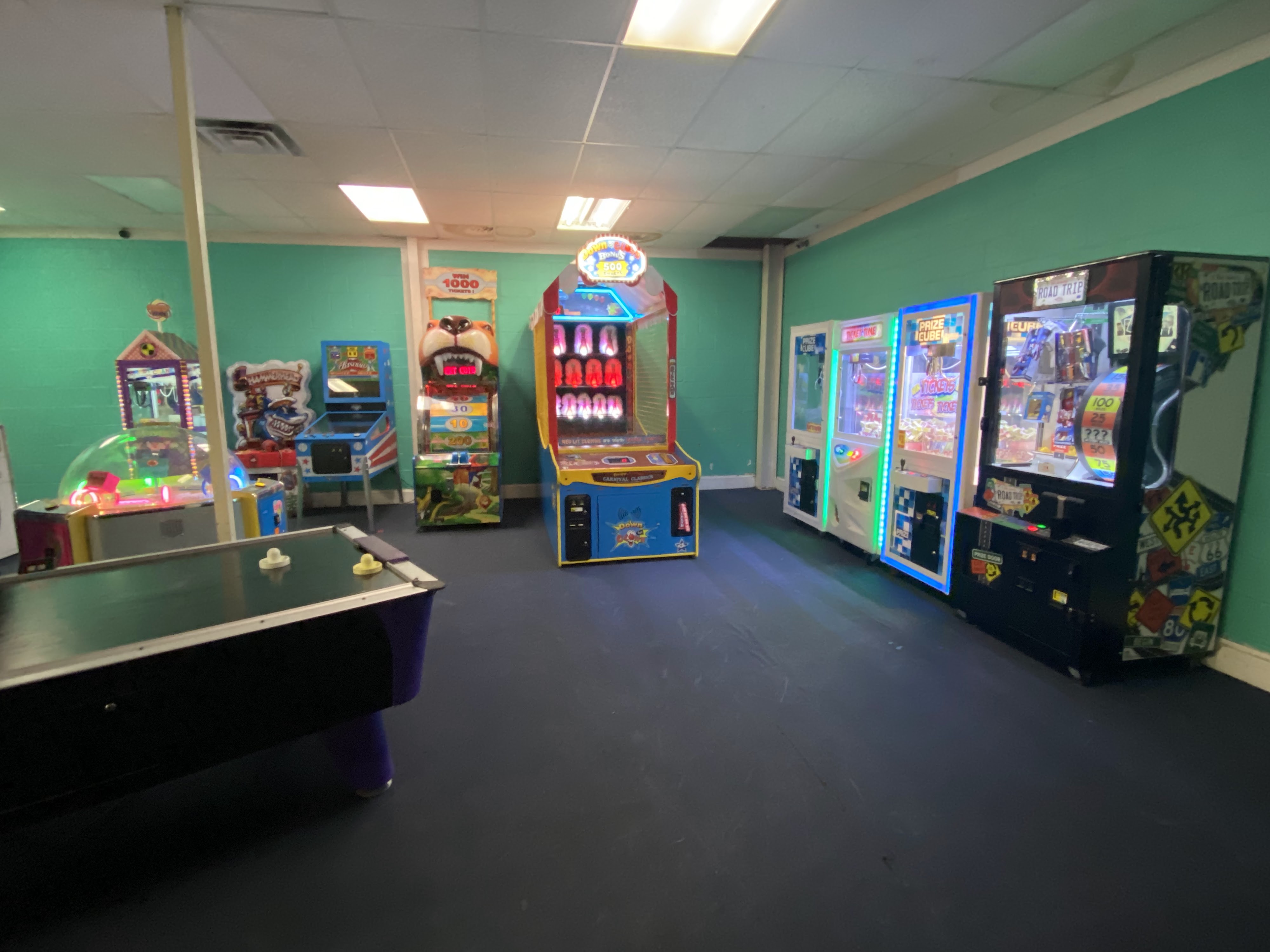 An arcade room with an air hockey table and several colorful ticket redemption machines against teal walls.