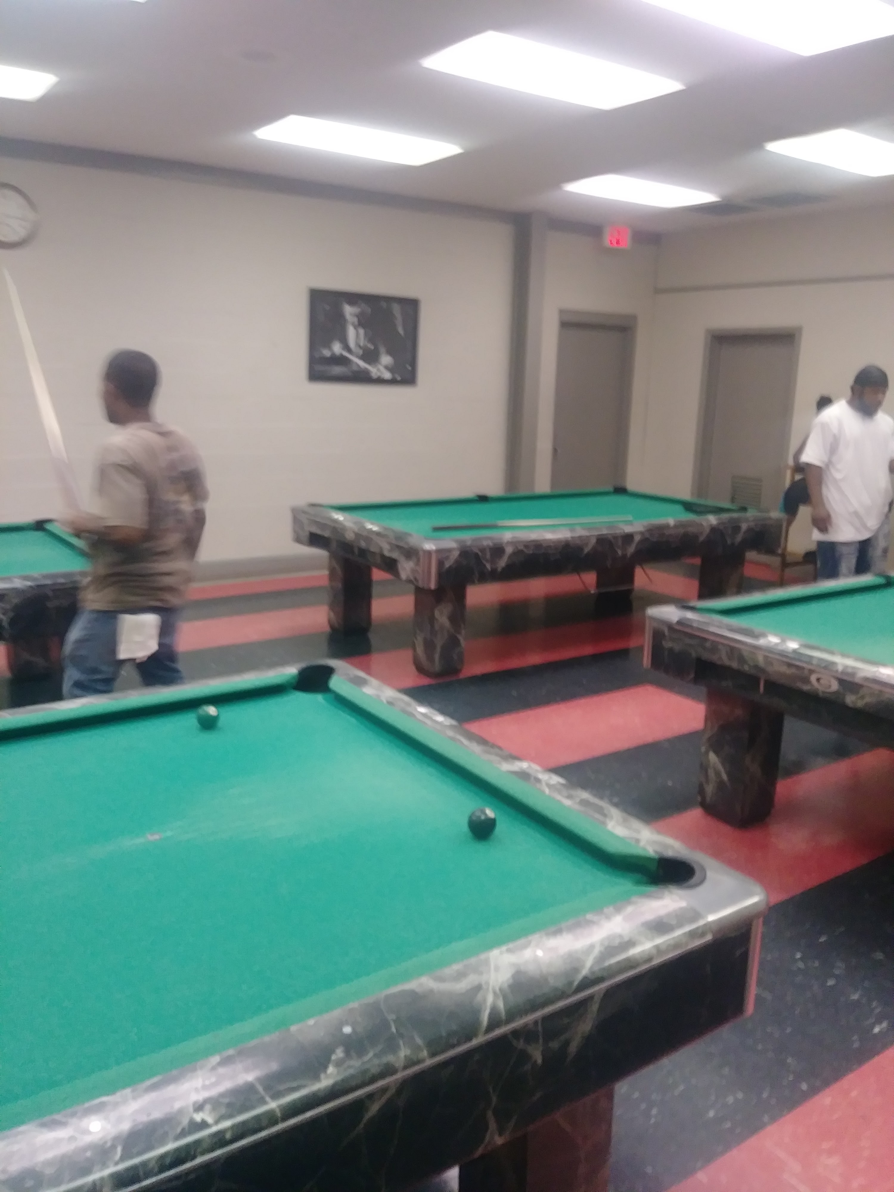Several green felt billiard tables in a room with red and black striped flooring.