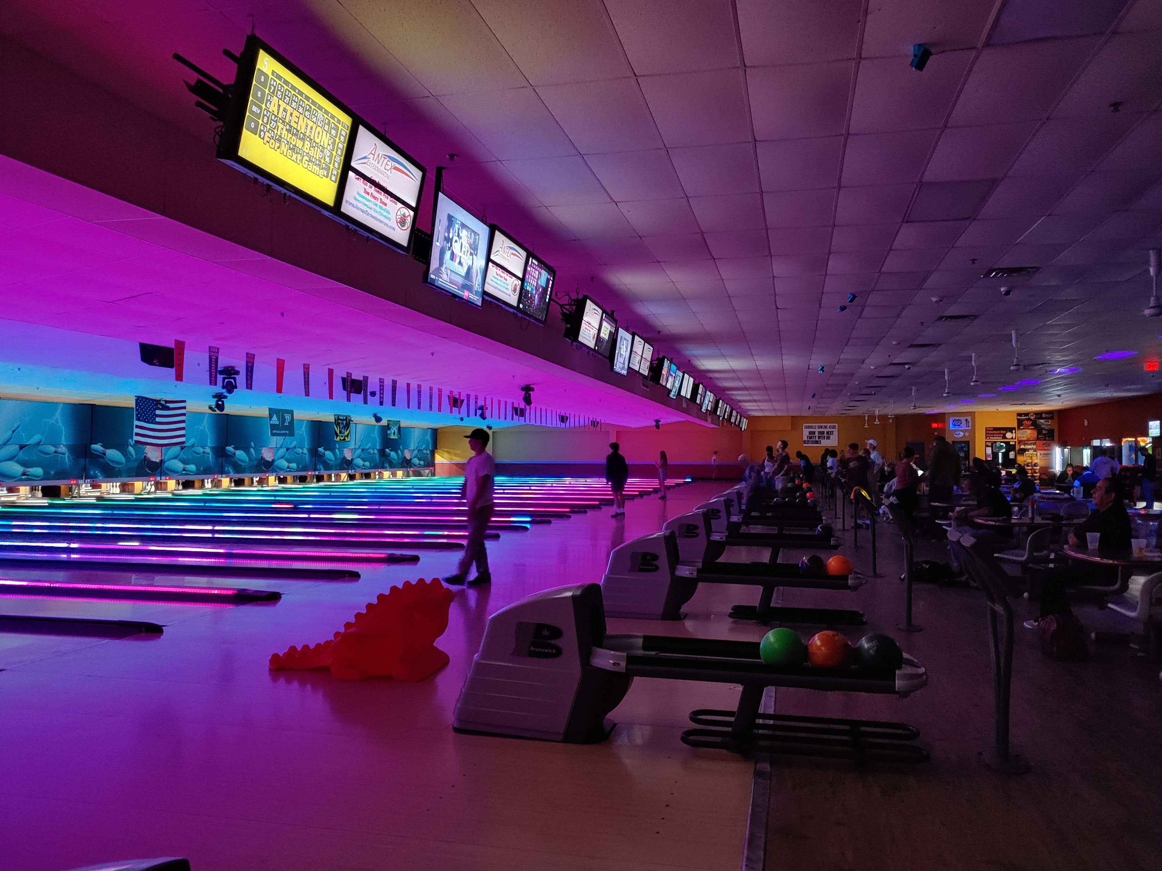 Vibrant bowling lanes lit with pink and blue LED lights during a cosmic bowling session at a modern center.
