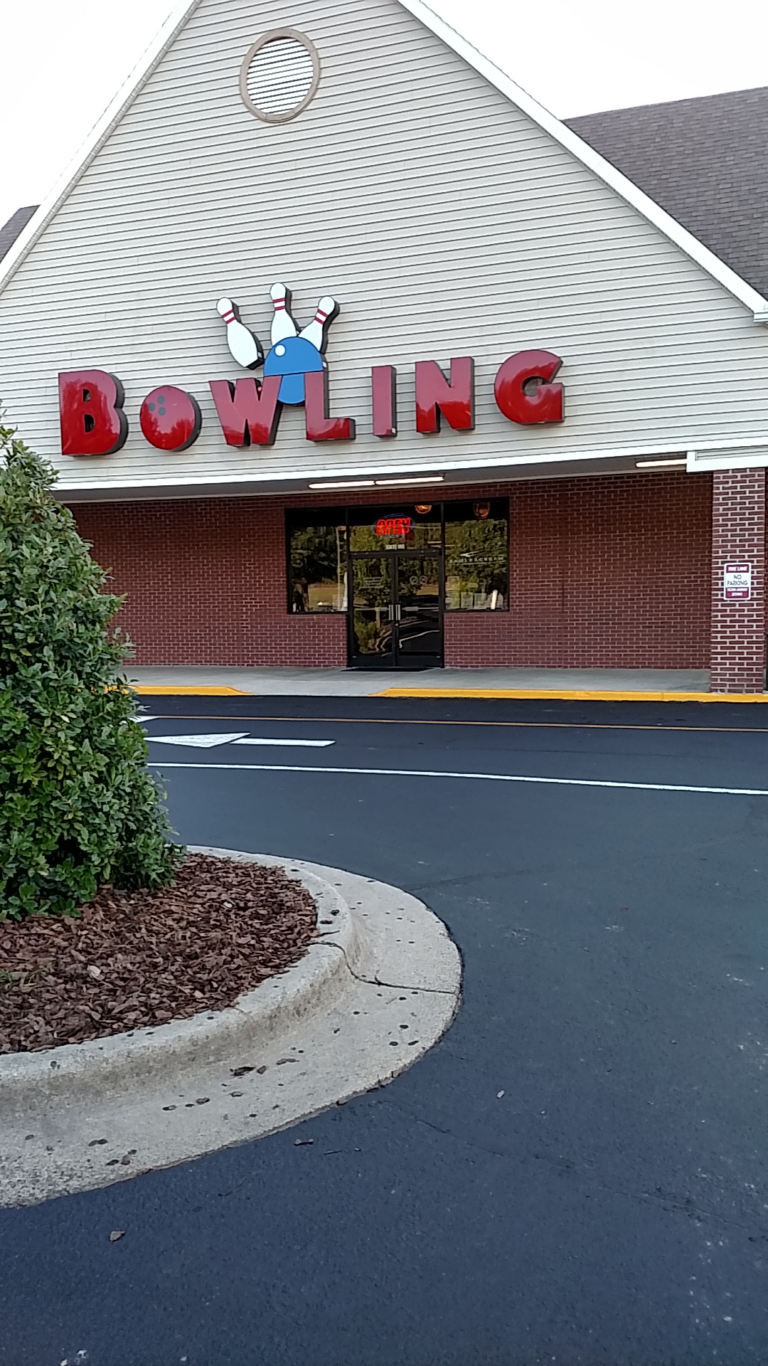 Exterior view of a bowling center with a large red sign above a brick and tan building.
