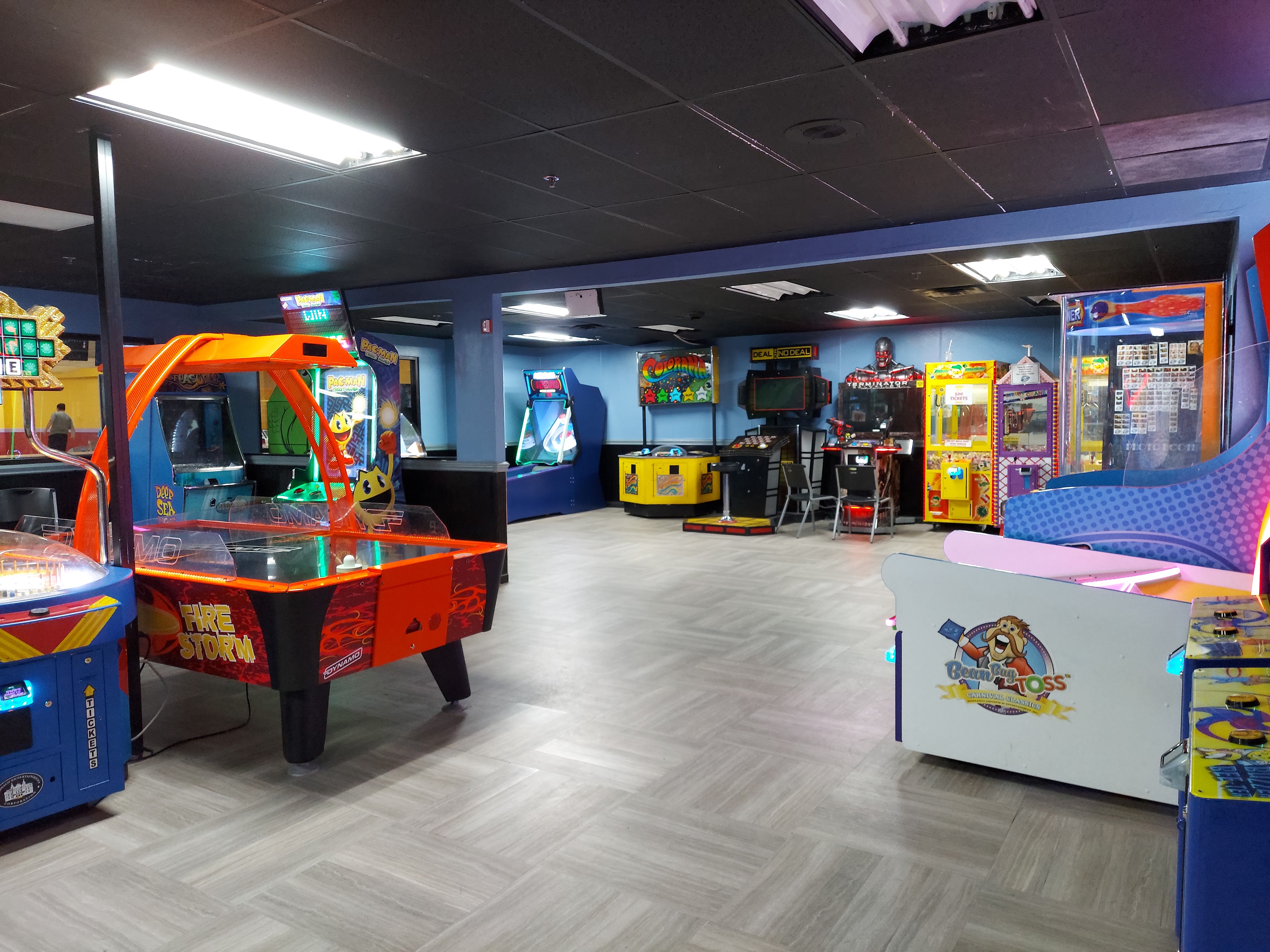 A clean, well-lit arcade area with an air hockey table in the foreground and various arcade cabinets in the background.