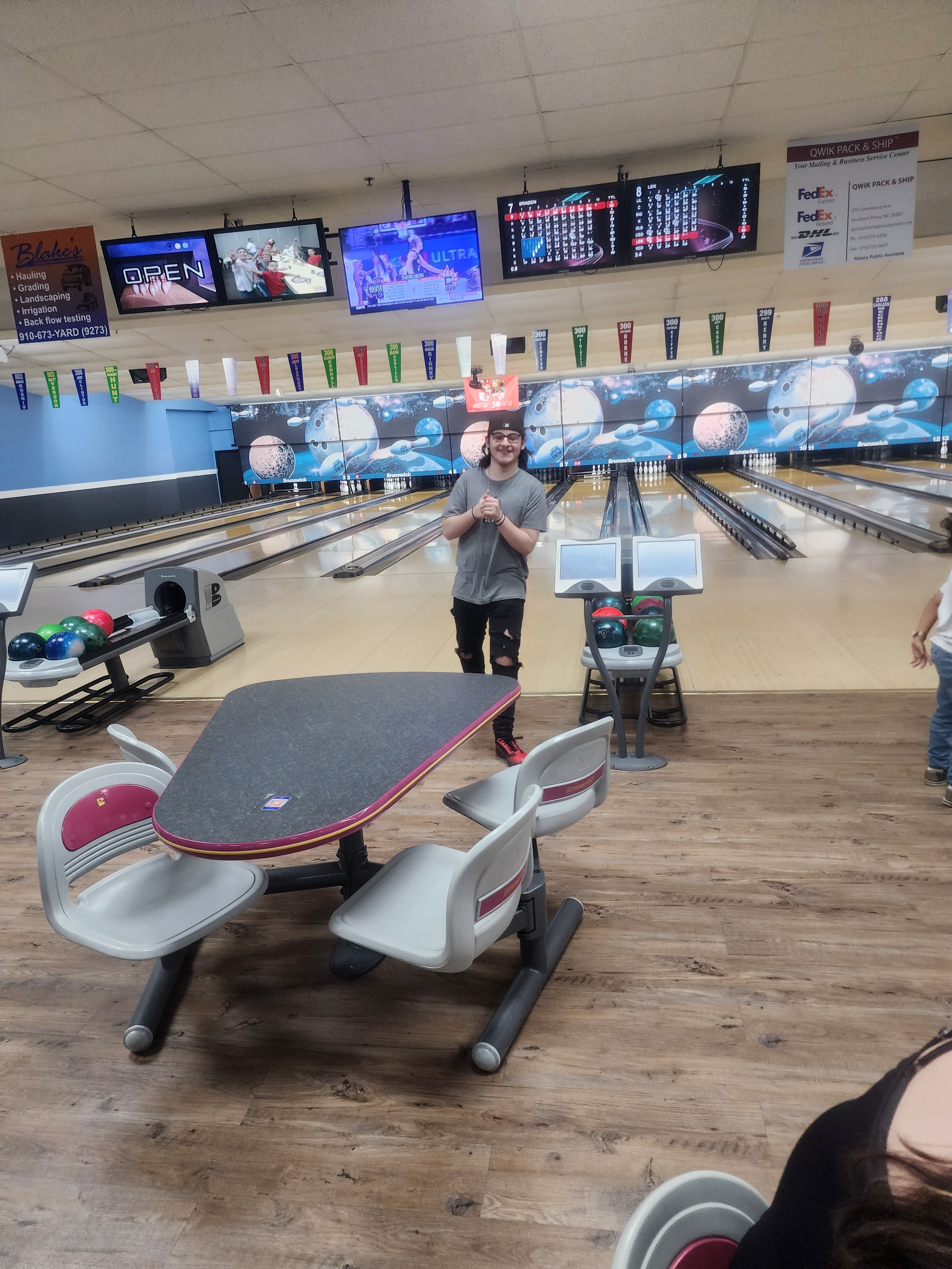 A person standing near bowling lanes with a triangular table and scoring monitors visible.